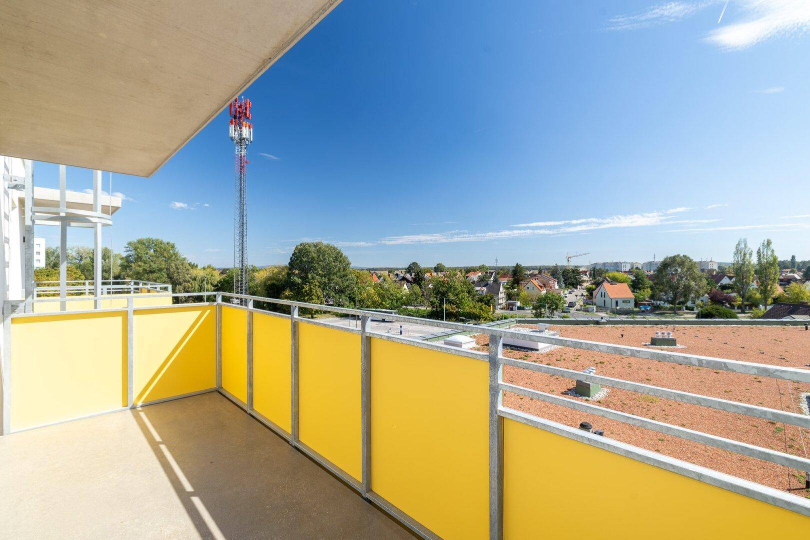 Balkon mit gelbem Geländer und Blick auf die Umgebung sowie einen Mobilfunkmast.