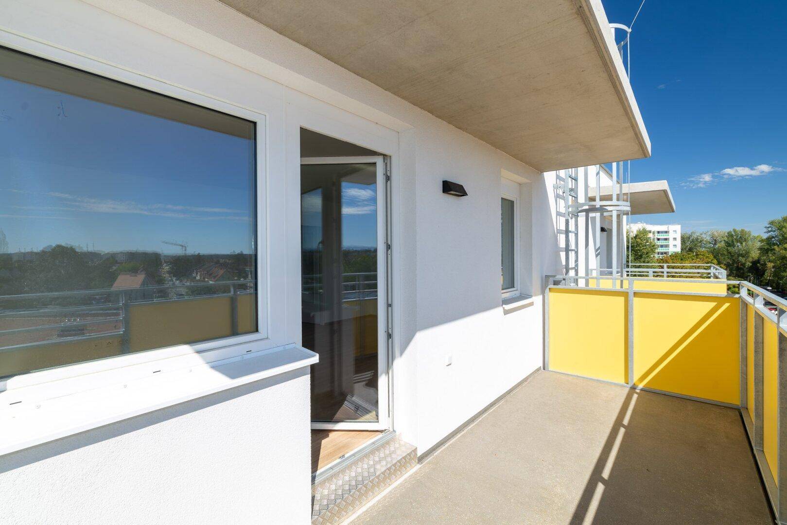 Heller Balkonbereich mit weißer Fassade und Zugang zu den Innenräumen der Wohnung.