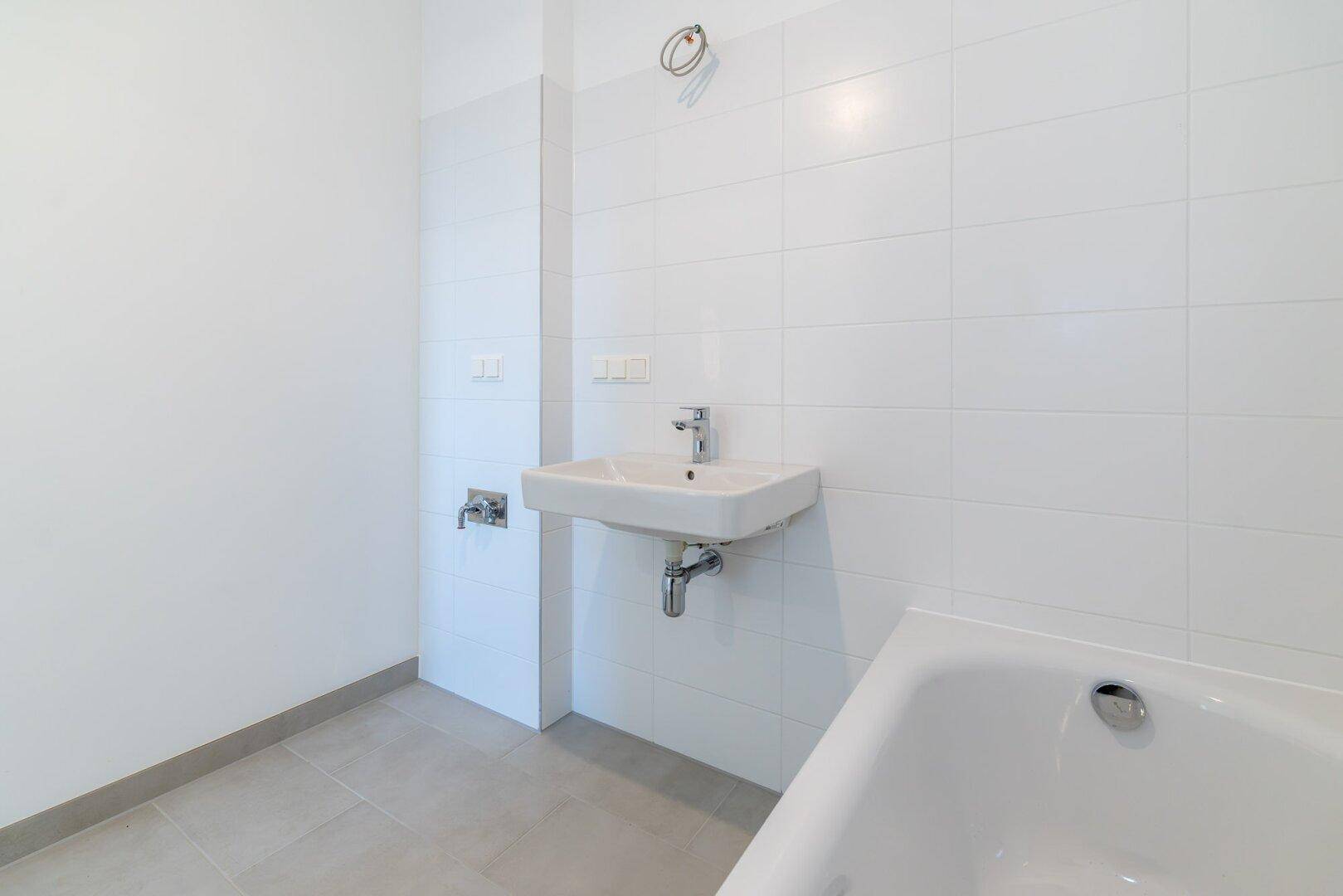 Modernes Badezimmer mit weißen Fliesen, Badewanne und Waschbecken.