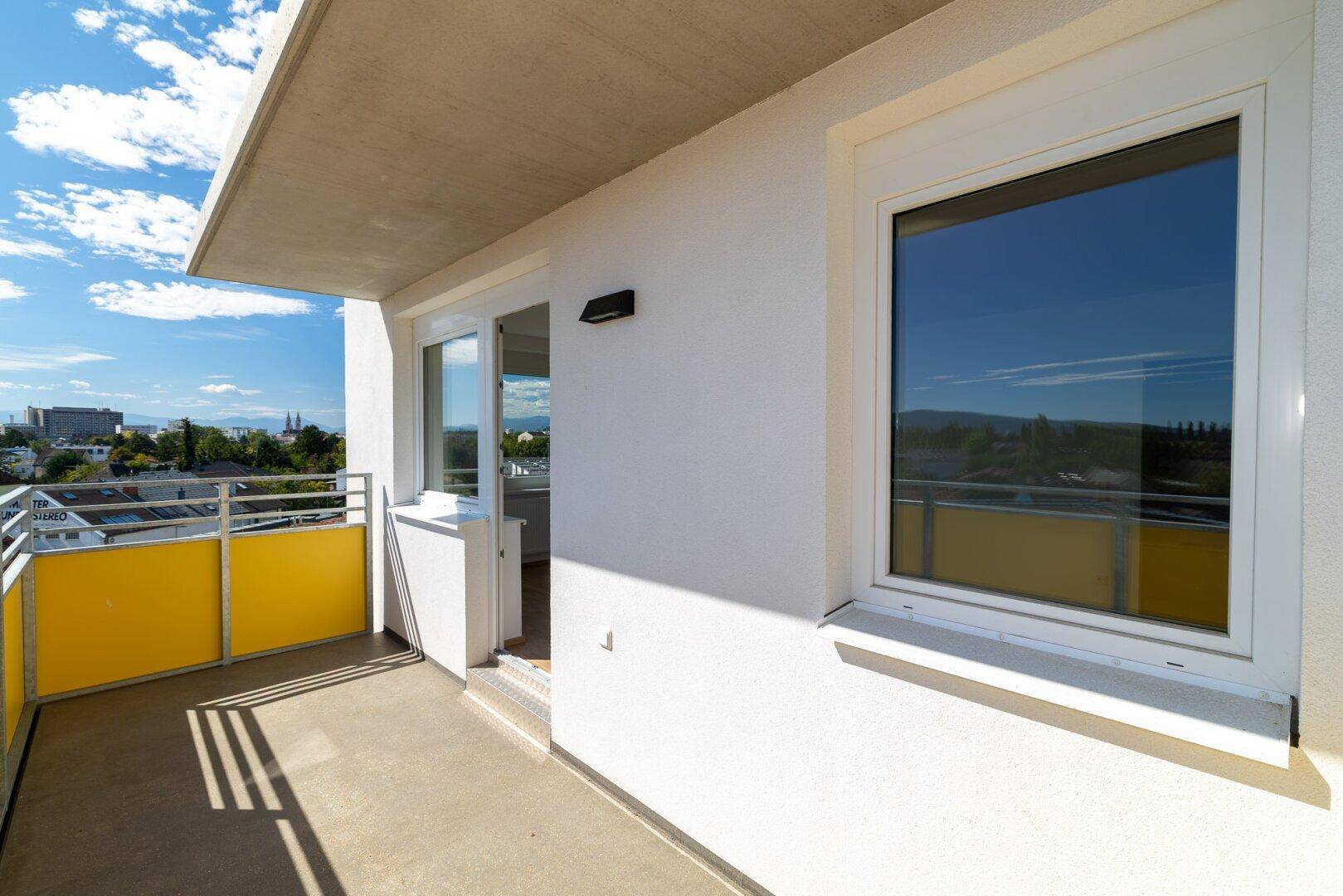 Sonniger Balkon mit weißer Fassade und weitem Blick über die Stadt und die Landschaft.