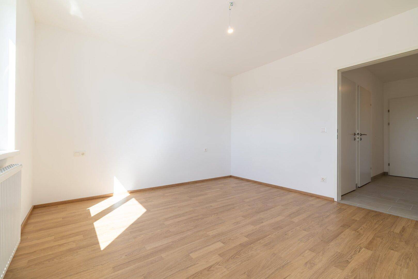 Helles Schlafzimmer mit Laminatboden, weiß gestrichenen Wänden und Zugang zum Flur.