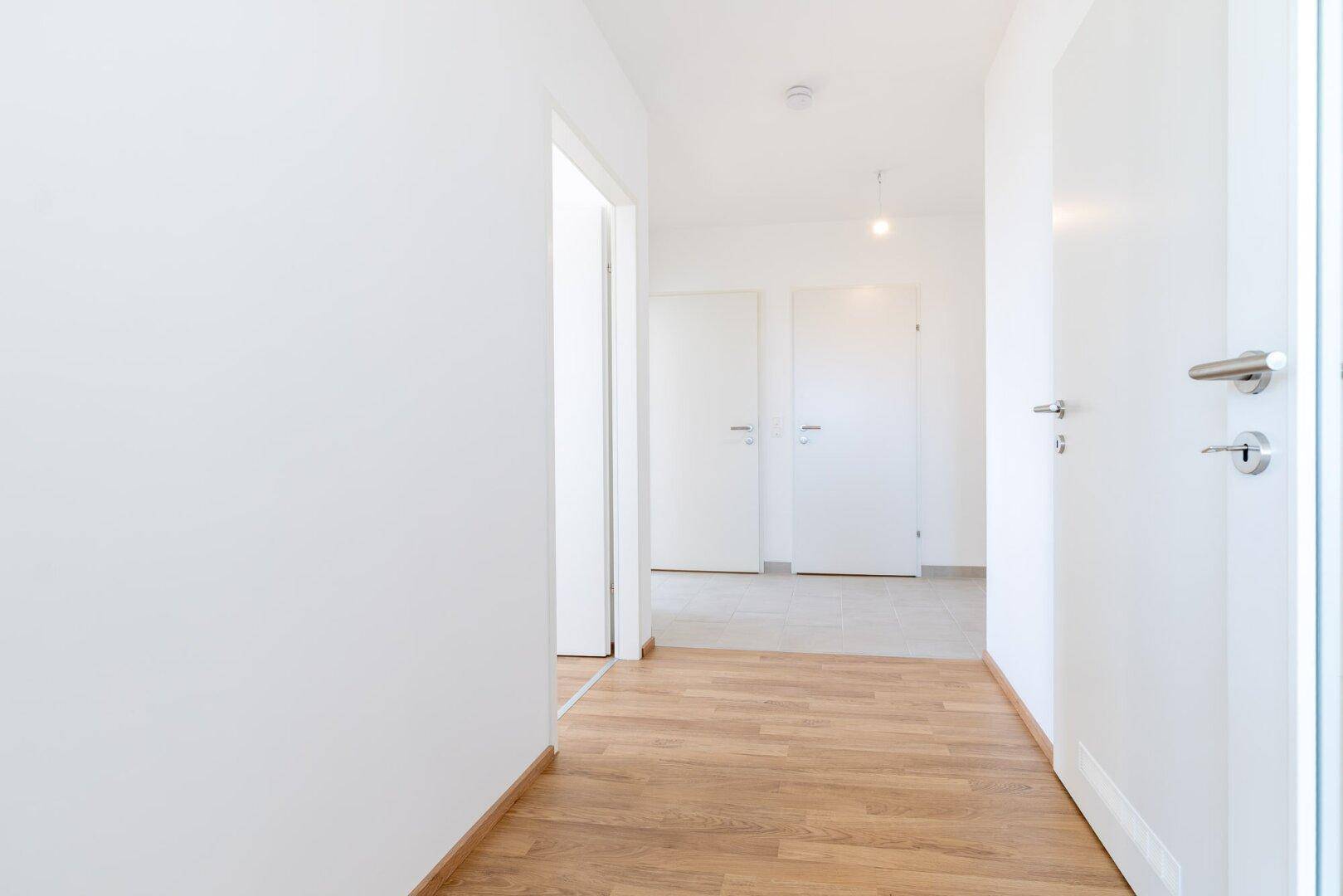 Heller Flur mit Laminatboden, weißen Wänden und mehreren Türen zu den angrenzenden Räumen.