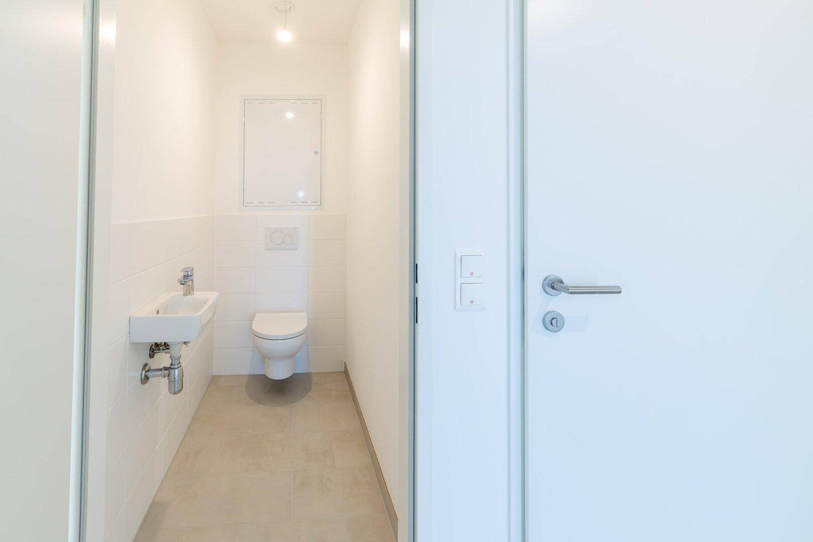 Modernes Gäste-WC mit weißen Fliesen, wandhängendem WC und kleinem Waschbecken.