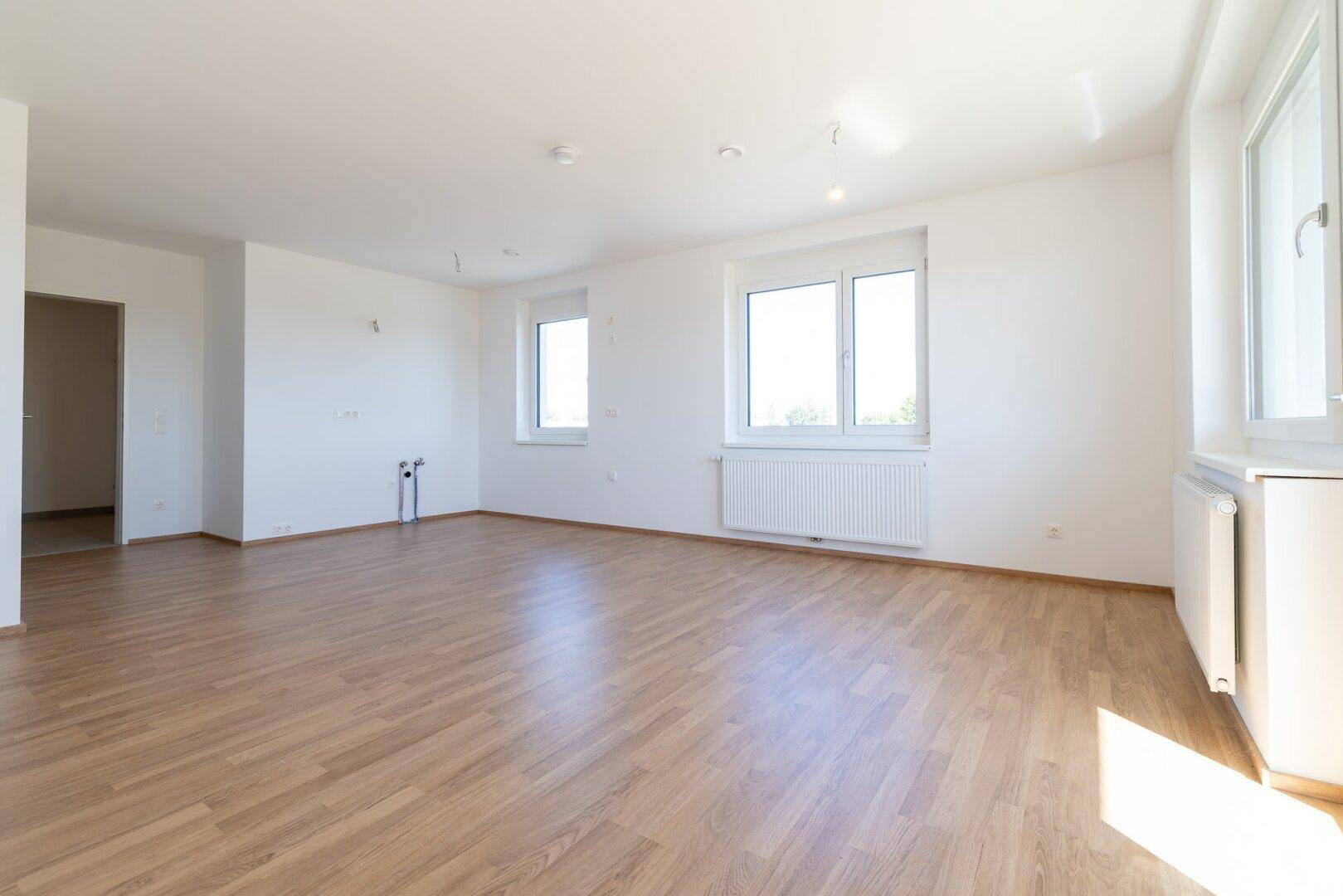 Lichtdurchfluteter Wohnbereich mit Laminatboden und weißen Wänden, bereit für die individuelle Gestaltung.