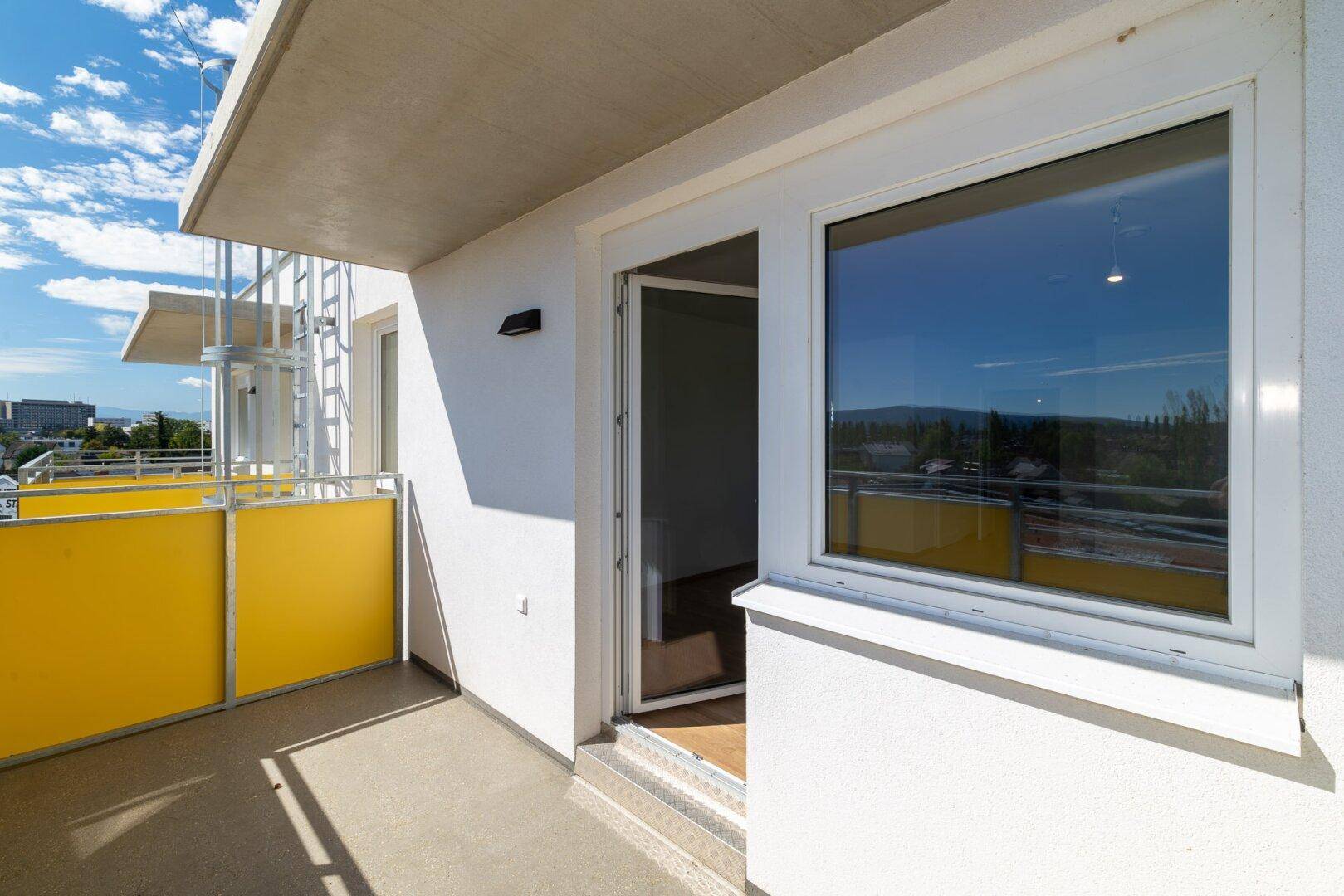 Sonniger Balkon mit gelben Brüstungselementen und Blick auf die umliegende Bebauung.