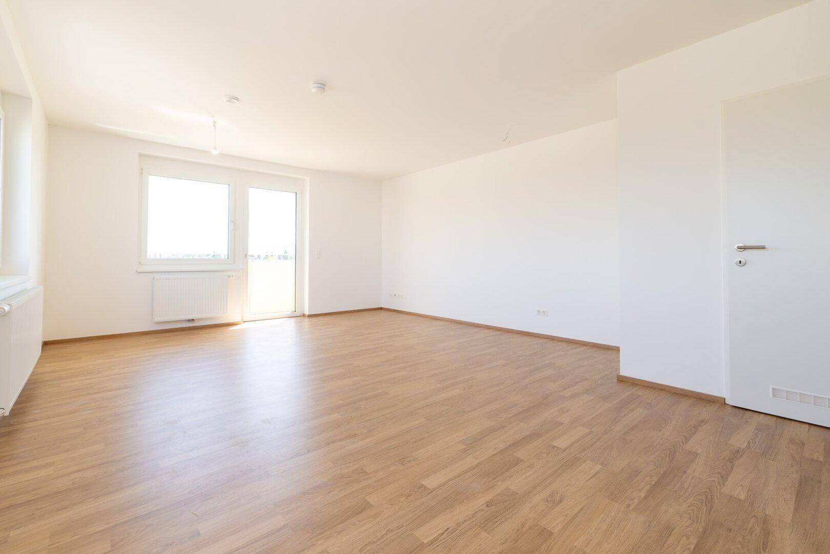 Heller Wohnraum mit Laminatboden, weißen Wänden und Zugang zu einem Außenbereich.