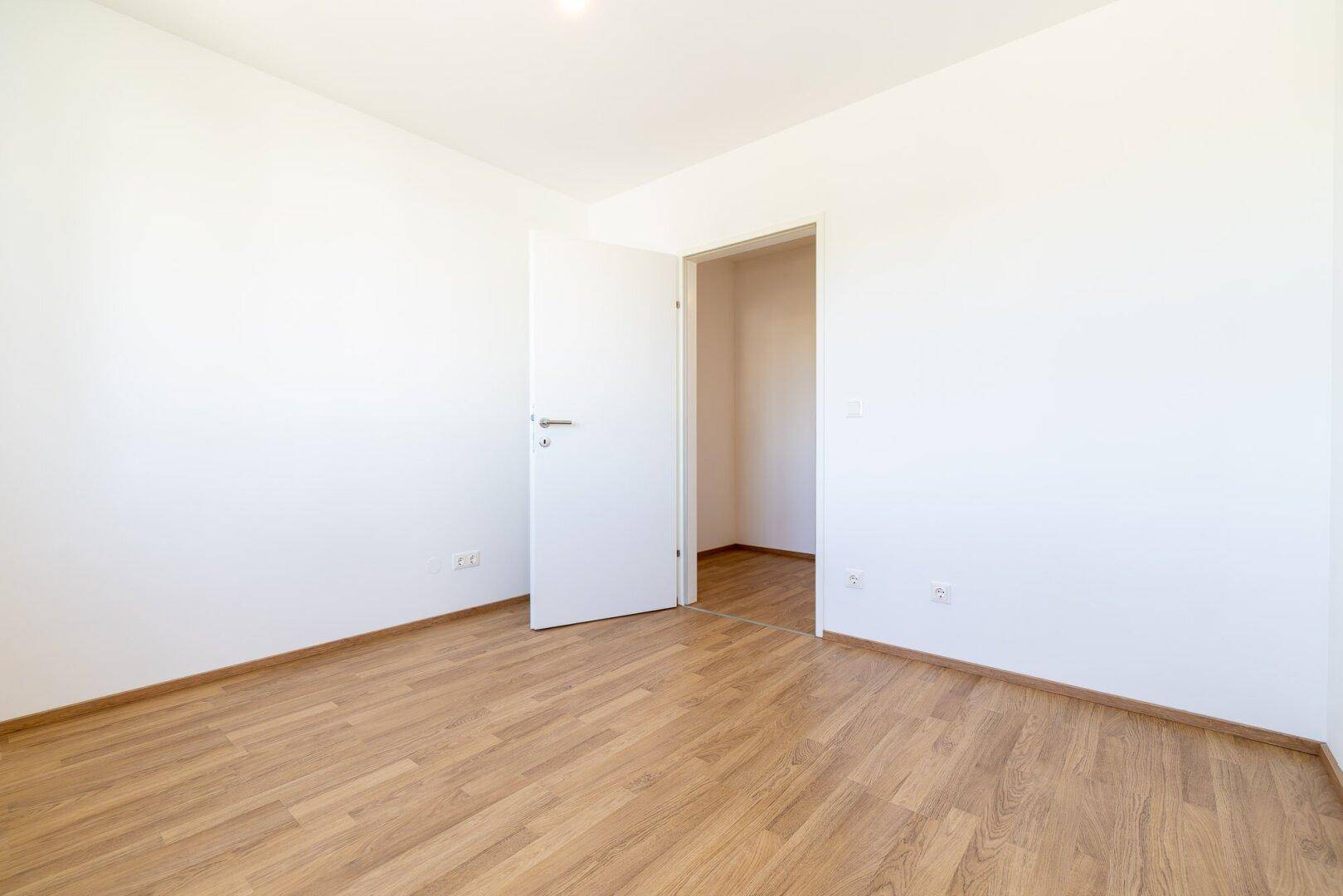 Schlafzimmer mit Laminatboden und weiß gestrichenen Wänden, bereit für individuelle Einrichtung.