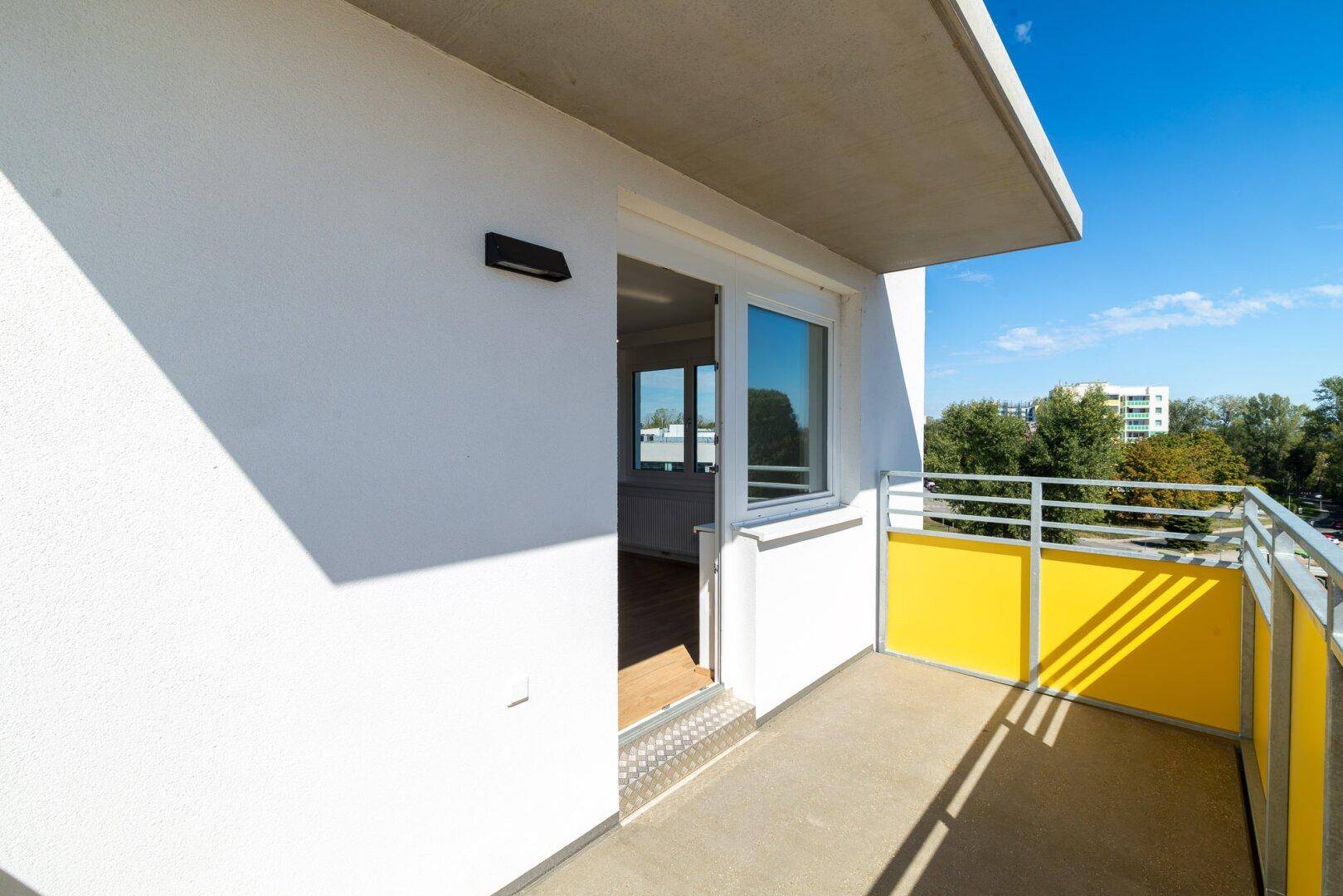 Balkon mit gelben Sichtschutzelementen und Zugang zum hellen Innenraum der Wohnung.