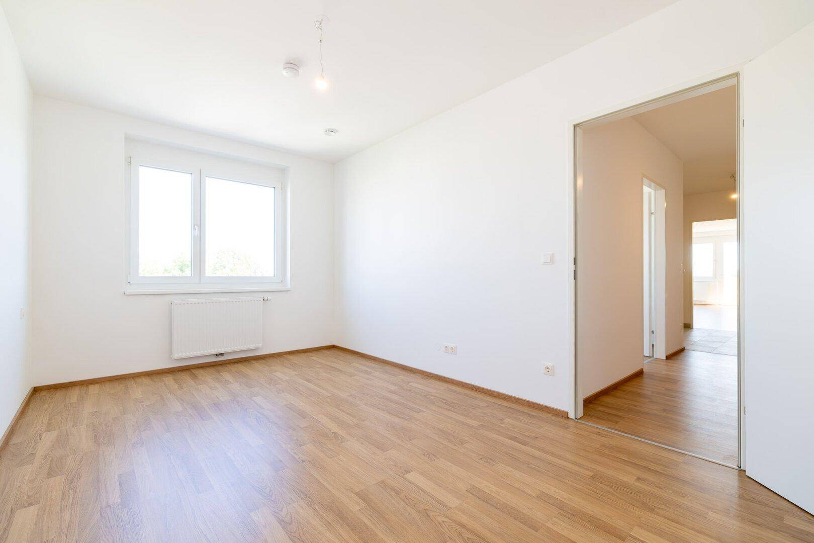 Geräumiges Schlafzimmer mit Laminatboden, großem Fenster und Schiebetür zum Flur.