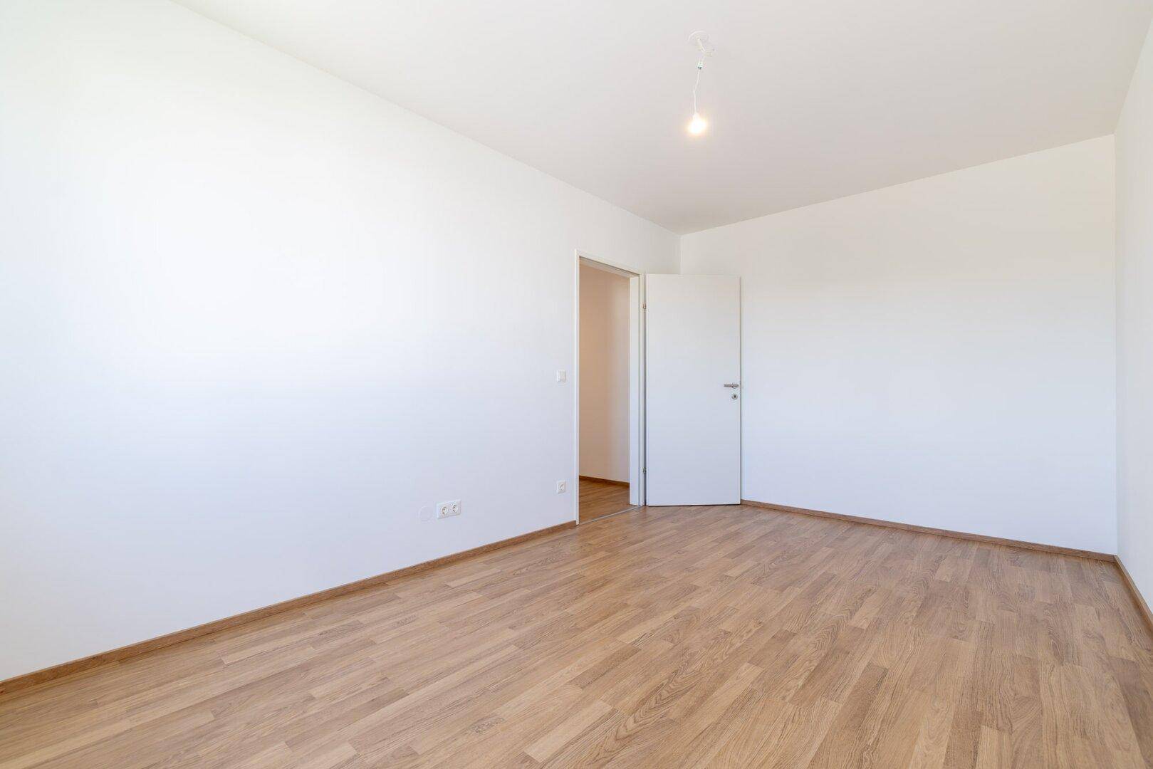Helles Schlafzimmer mit Laminatboden und weißen Wänden, ideal für eine ruhige Atmosphäre.