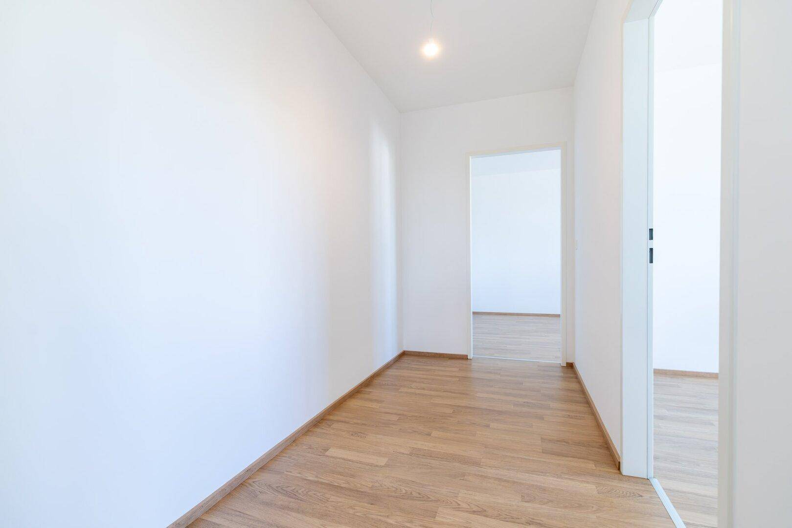 Heller Flur mit Laminatboden, weißen Wänden und Zugang zu verschiedenen Räumen.