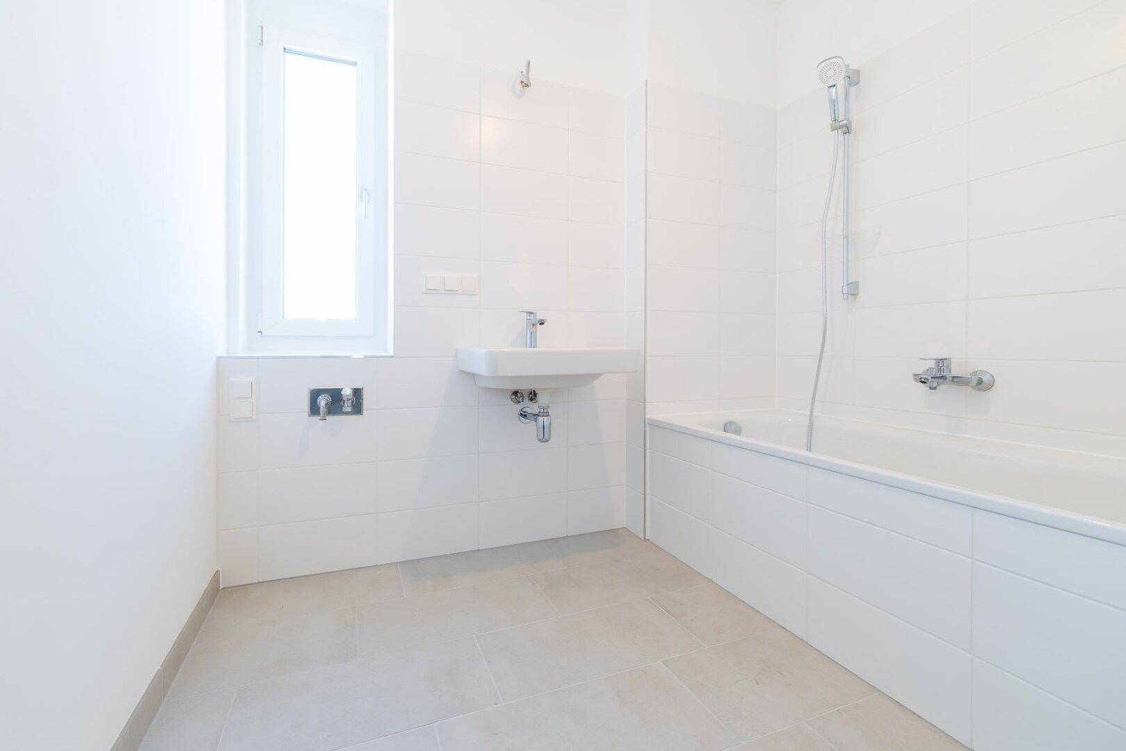 Modernes Badezimmer mit weißen Fliesen, Badewanne, Waschbecken und Fenster für Tageslicht.