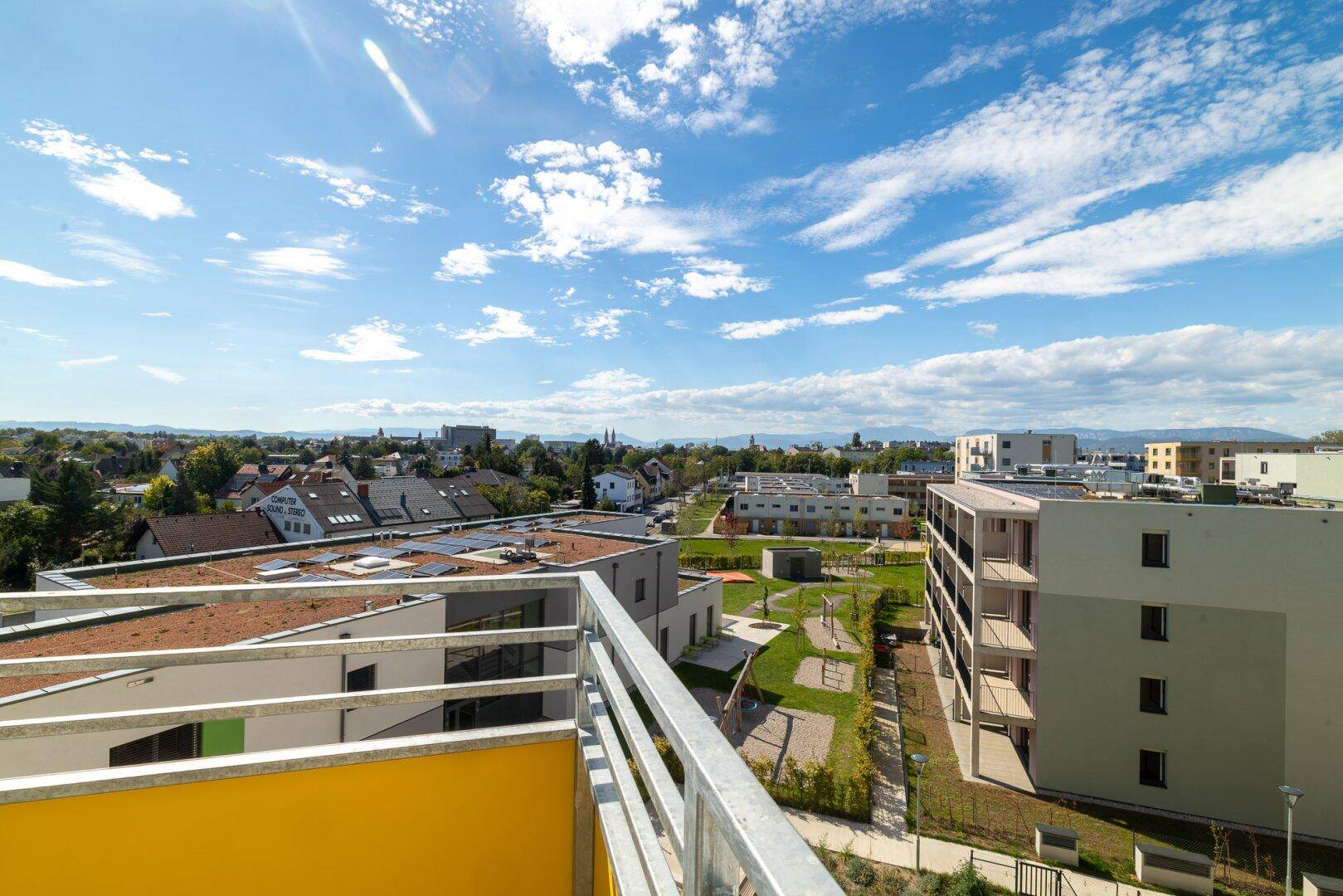 Weitläufiger Ausblick vom Balkon über die umliegende Wohngegend mit Grünflächen und blauem Himmel.