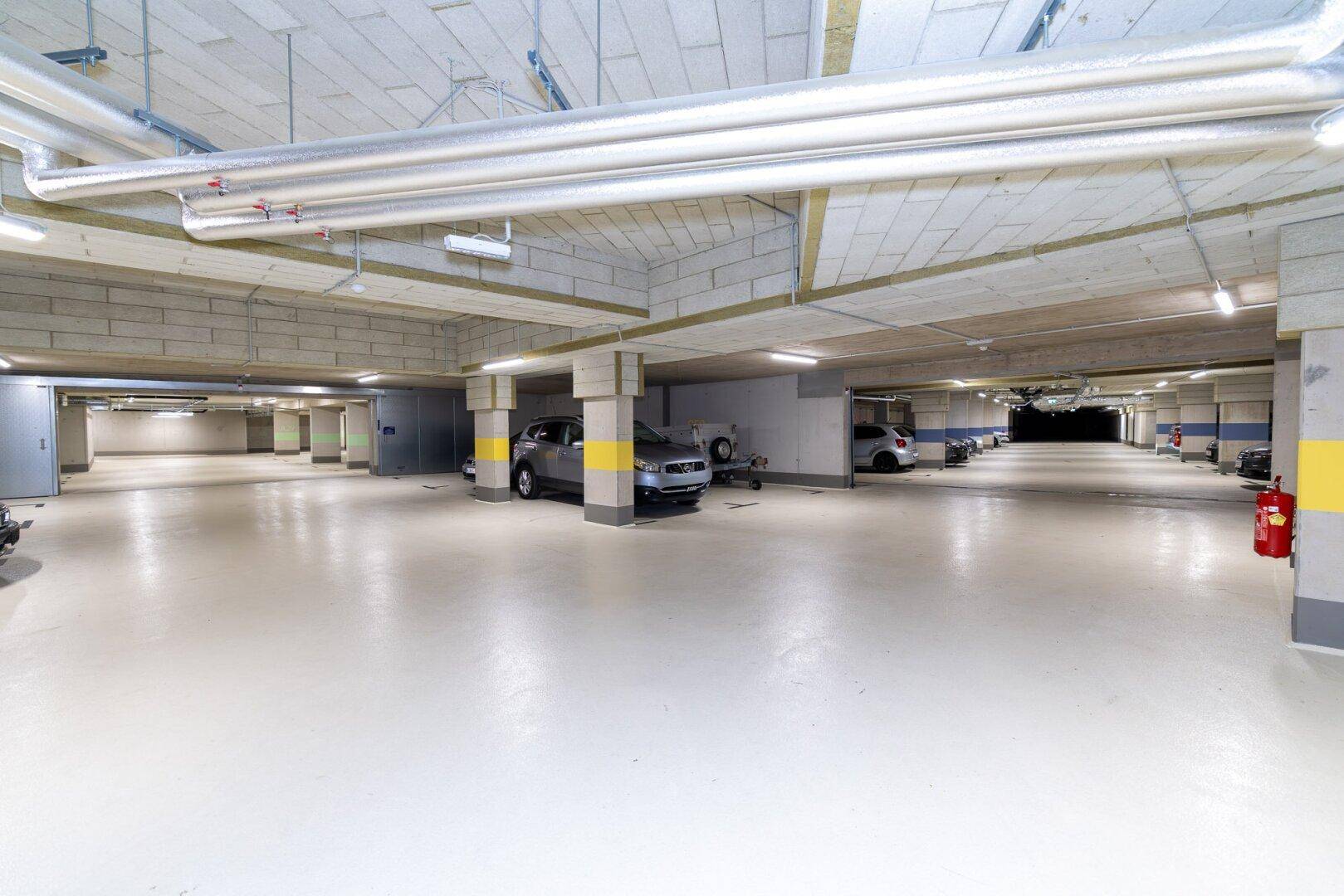 Weitläufige Tiefgarage mit zahlreichen Stellplätzen, Betonpfeilern und moderner Beleuchtung.