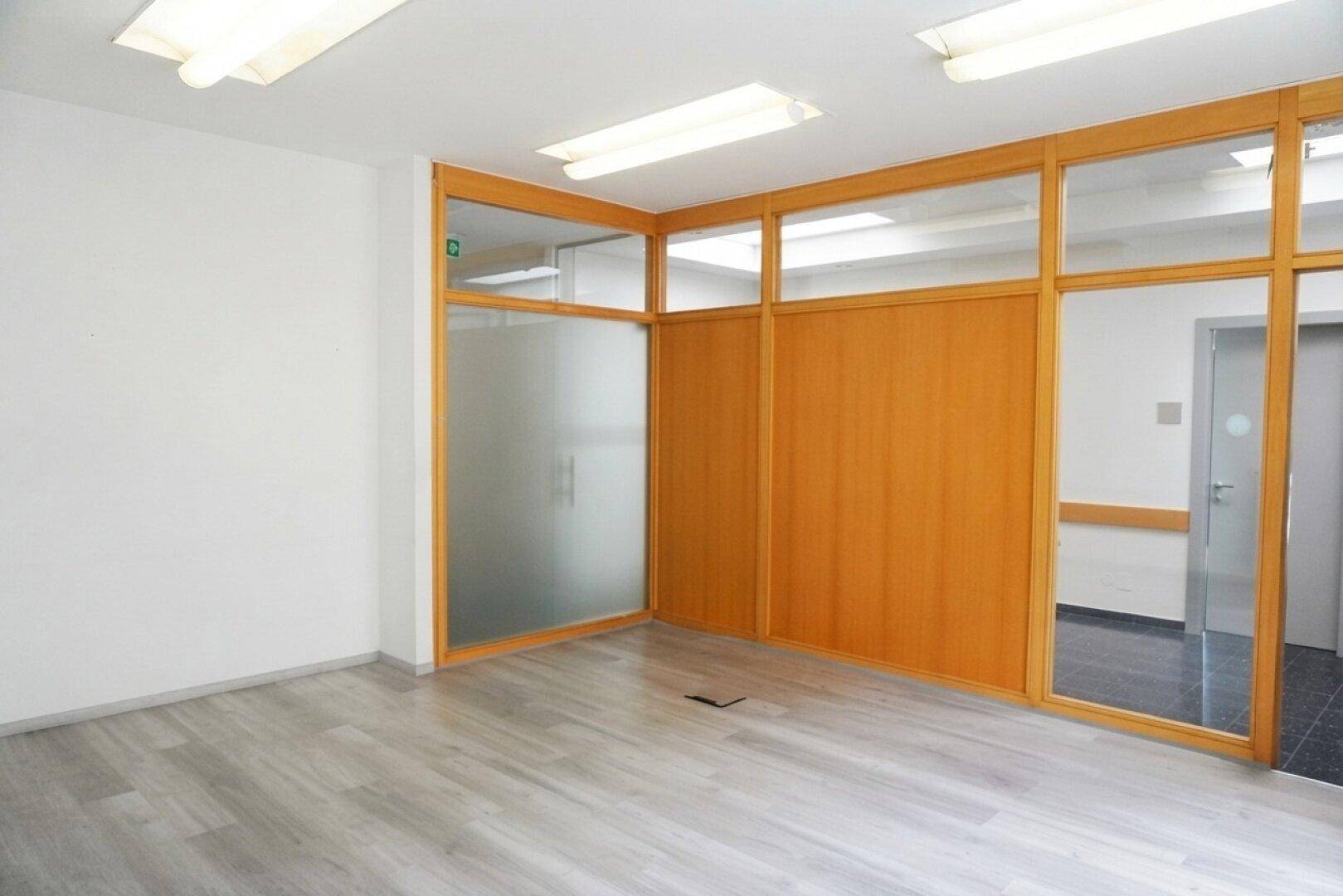 Leeres Büro mit hellem Laminatboden und Holz-Glas-Trennwänden, bereit zur individuellen Gestaltung.