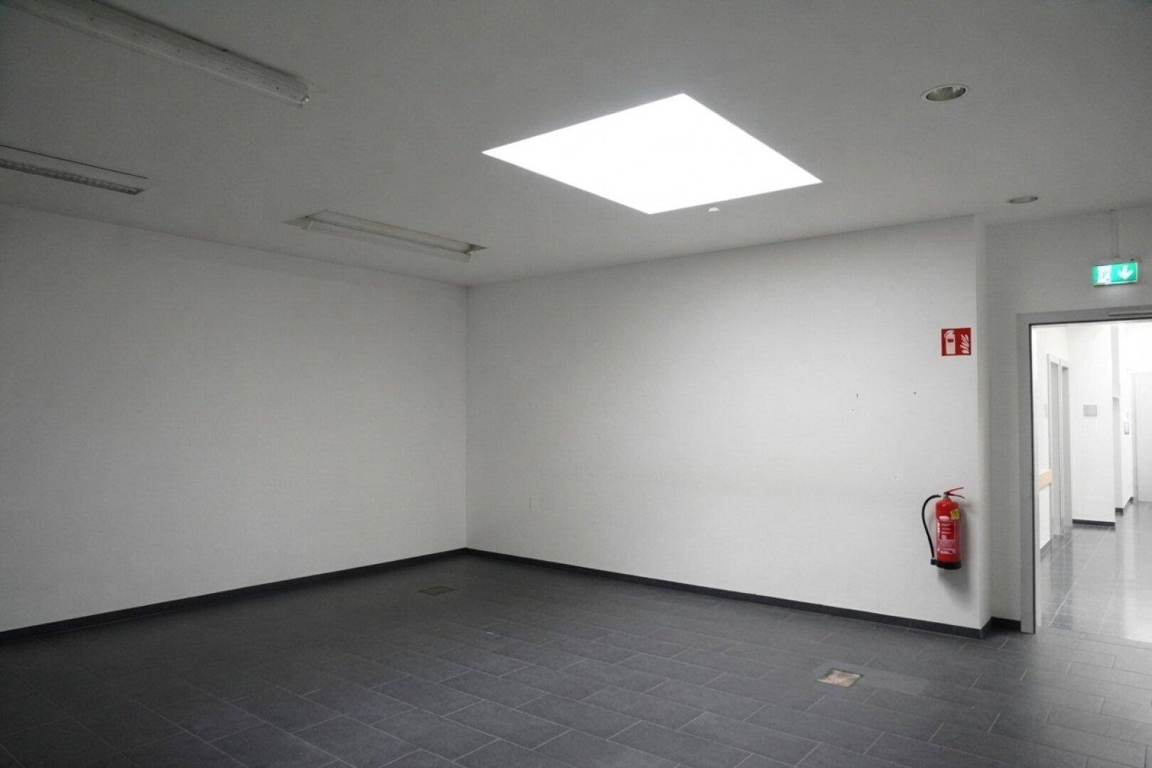 Heller Flur mit dunklem Fliesenboden und Oberlicht, führt zu weiteren Büroräumen im Gebäude.