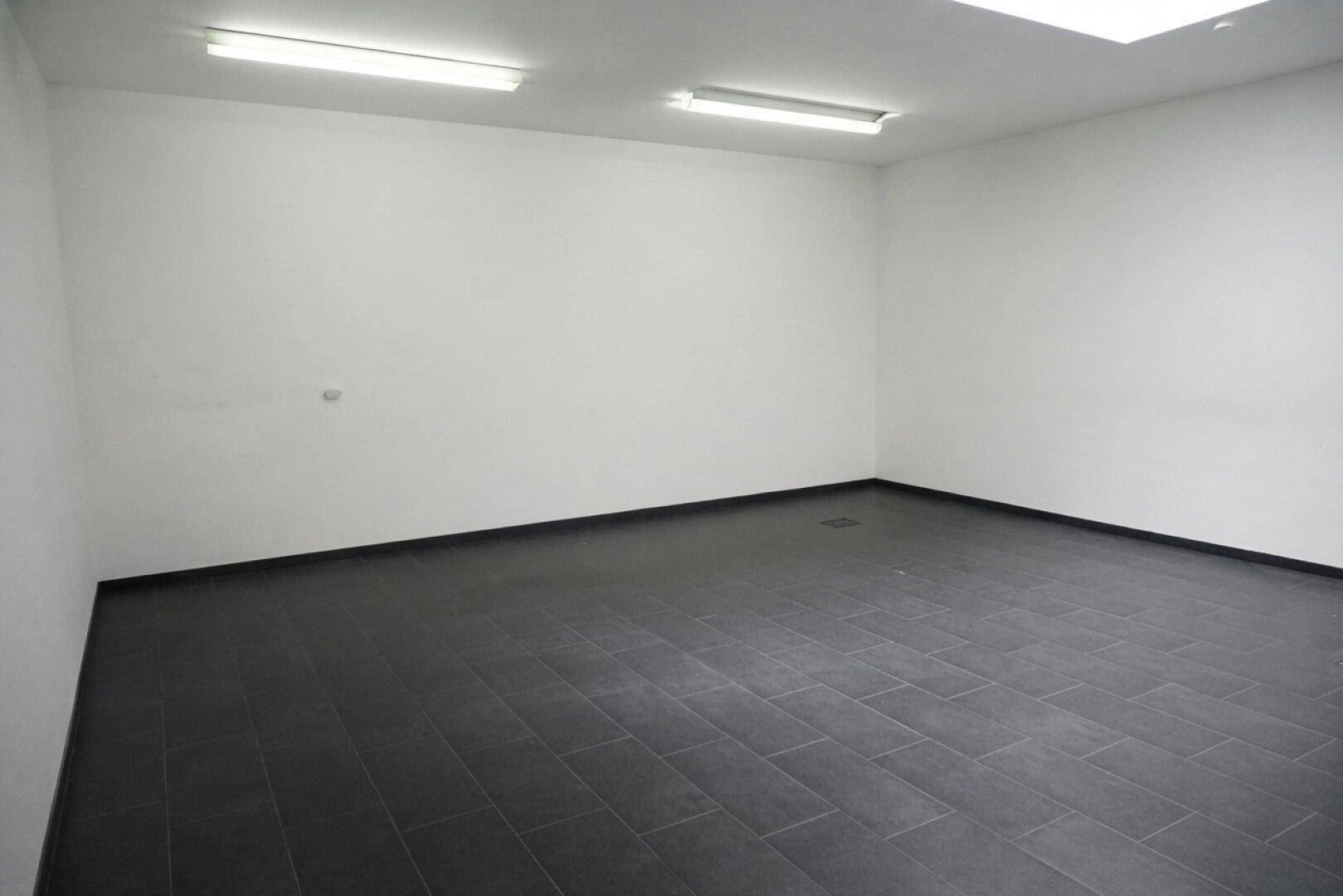 Geräumiger Büroraum mit dunklem Fliesenboden und weißen Wänden, ideal für flexible Büronutzung.