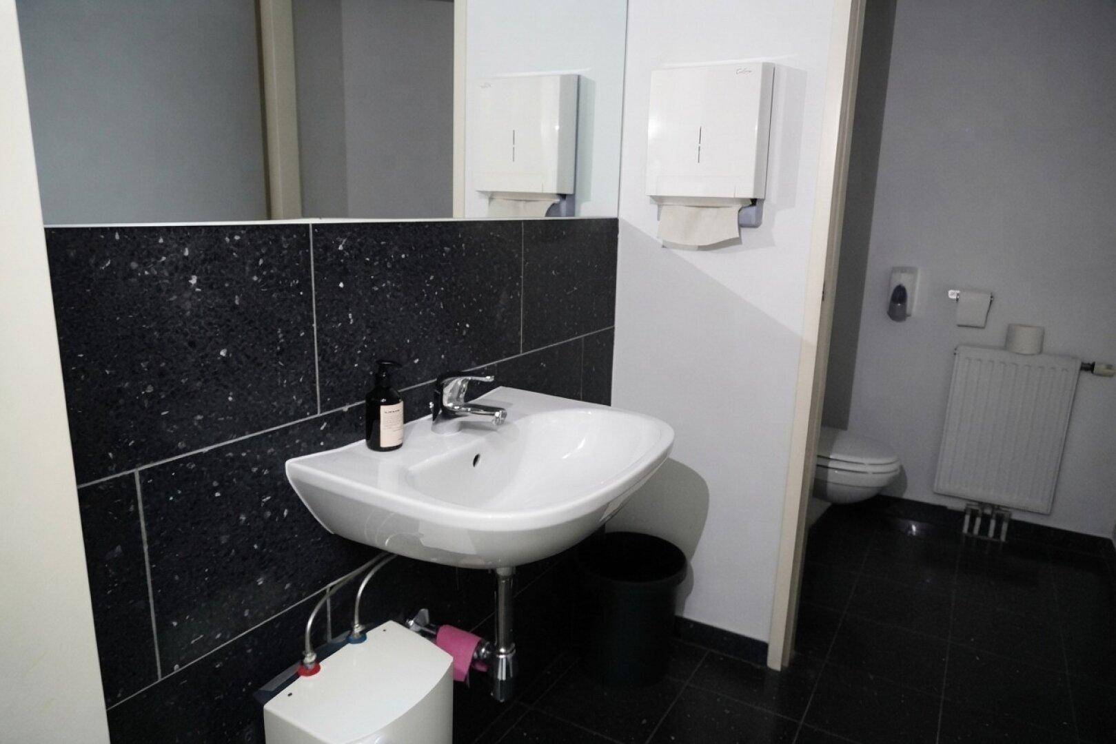 Modernes WC mit schwarzem Granitfliesen-Waschtisch und weißem Waschbecken, gut beleuchtet.