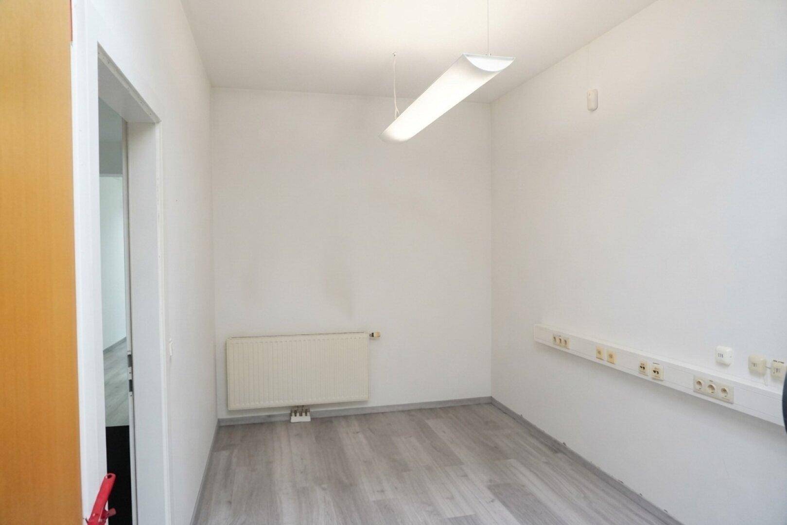 Helles Büro mit hellem Laminatboden und Heizkörper, bereit für die individuelle Einrichtung.