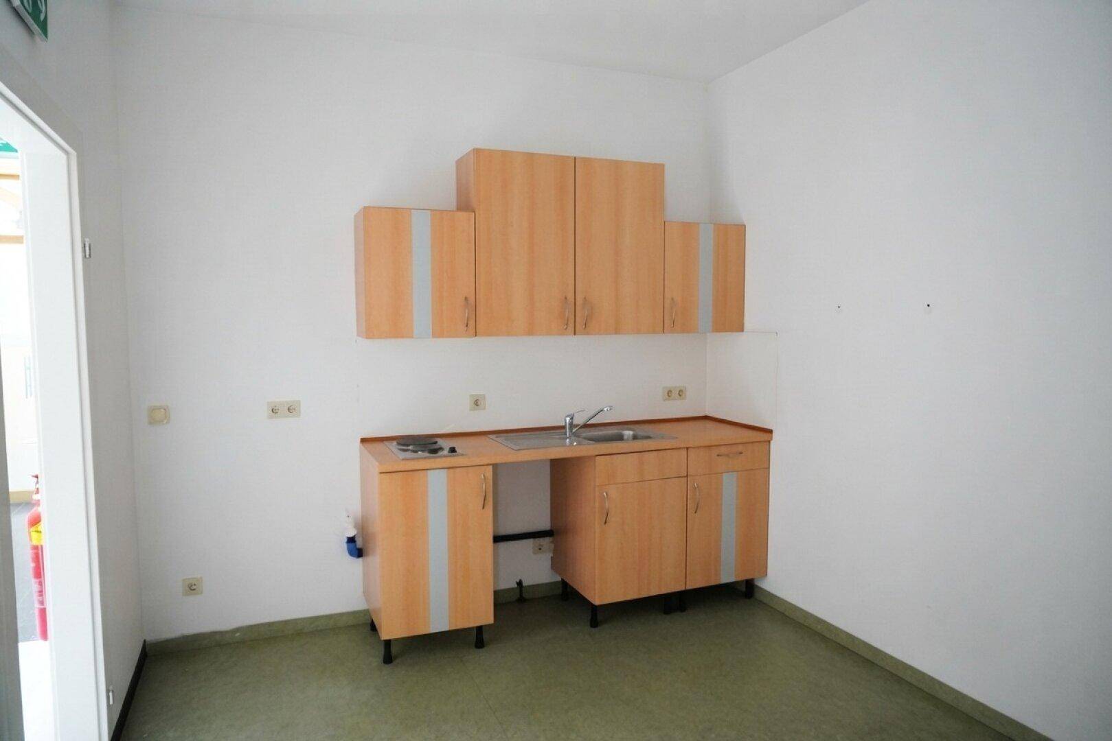Einfache Küchenzeile mit Holzschränken, Spüle und Kochplatte in einem kleinen Raum.