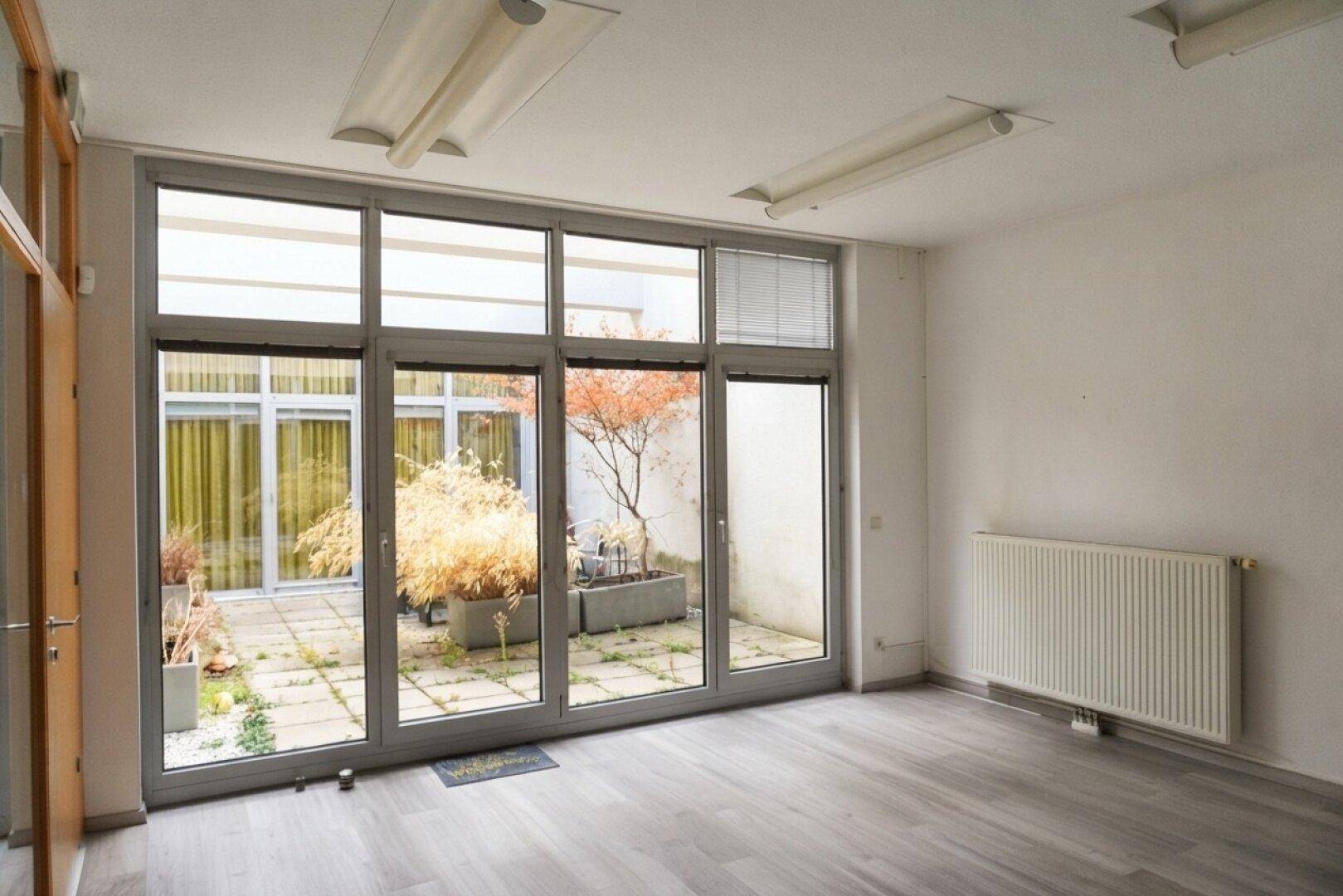 Heller Büroraum mit Laminatboden und großen Fenstern, die einen Blick auf den Innenhof bieten.