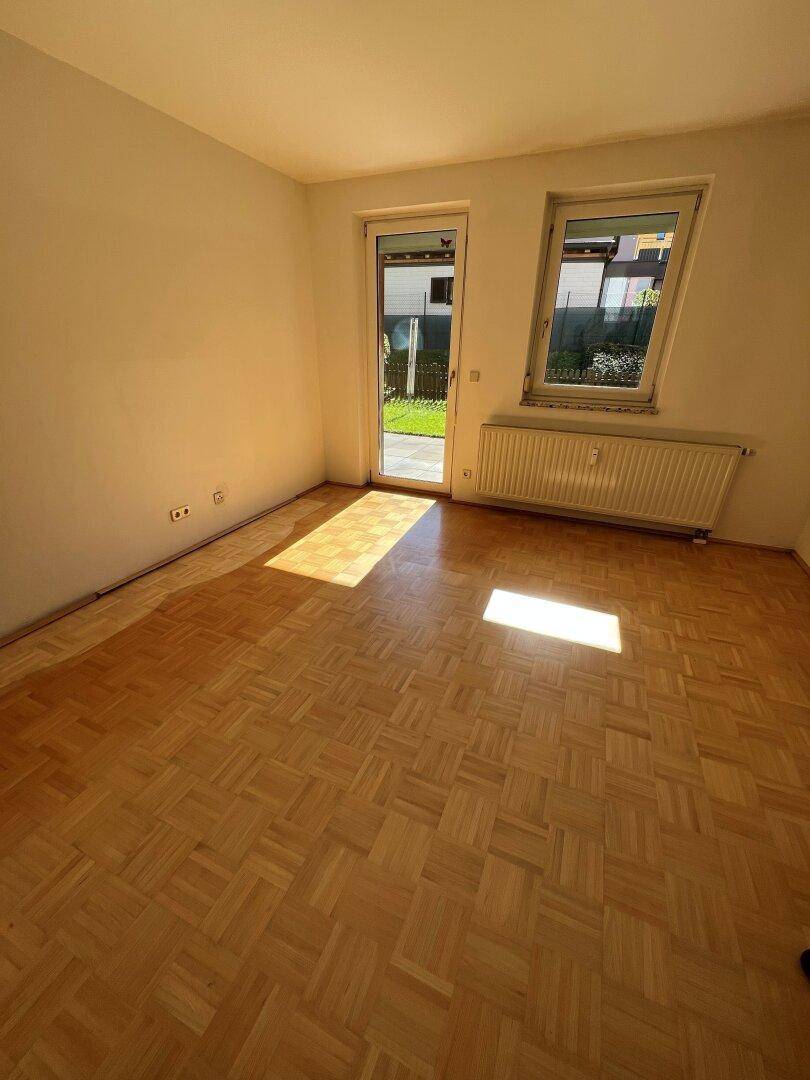 Heller Wohnraum mit Parkettboden und direktem Zugang zu einem Außenbereich, durchflutet von Sonnenlicht.