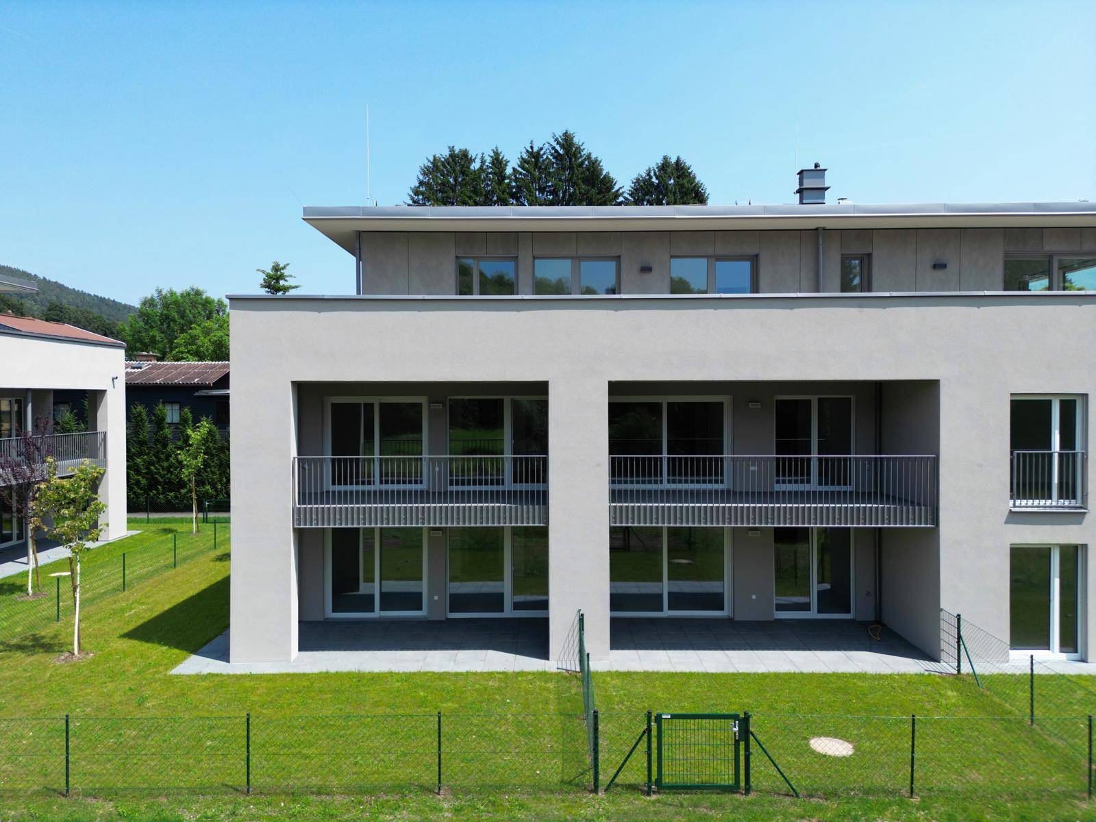 Moderne Gebäudefassade mit Balkonen und Terrassen, umgeben von einer gepflegten Rasenfläche.