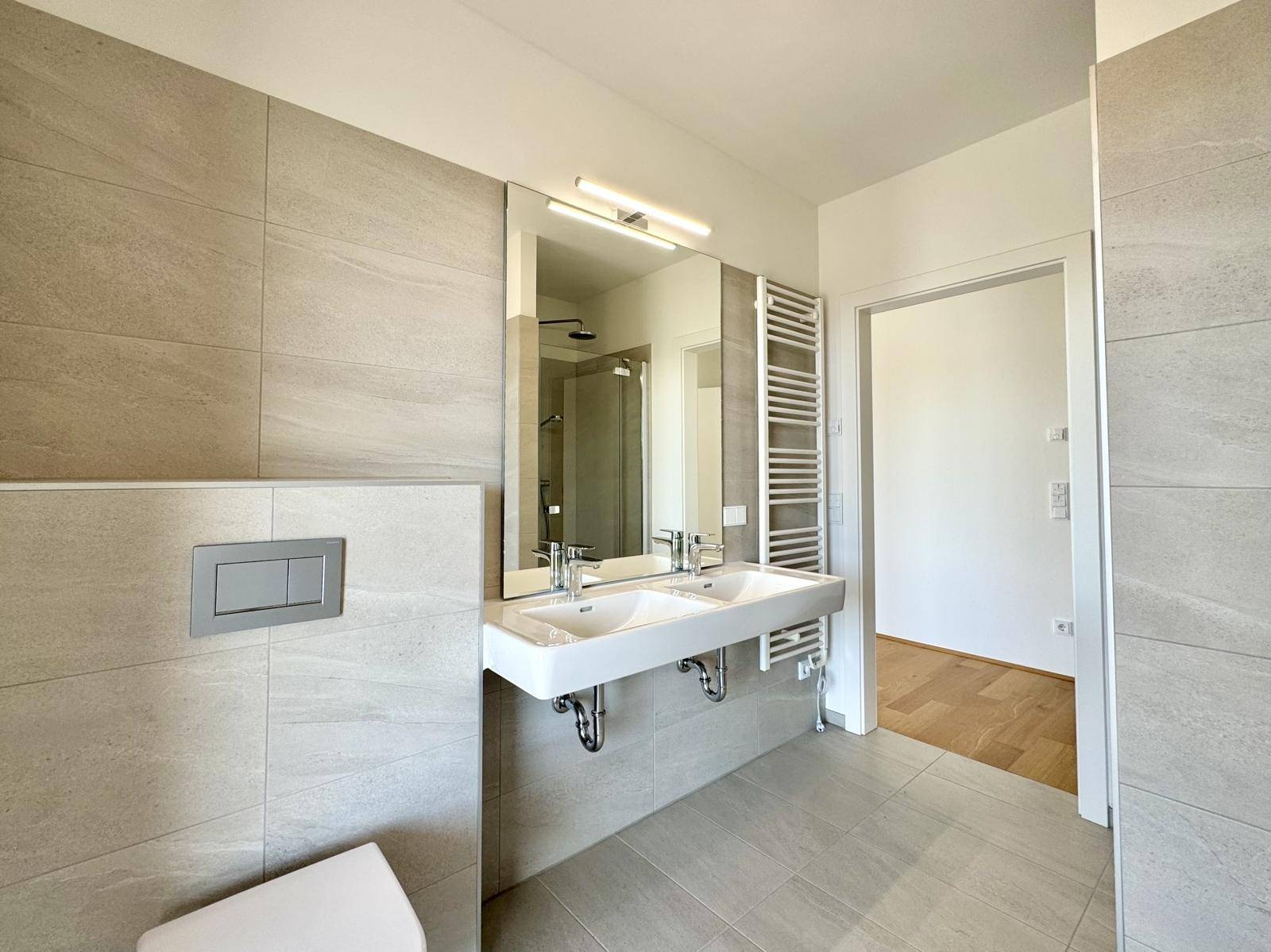 Geräumiges Badezimmer mit Doppelwaschbecken, großem Spiegel und modernen Fliesen.