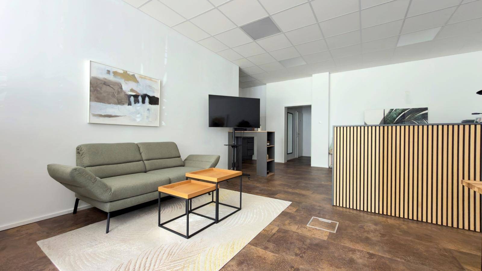 Gemütlicher Wartebereich mit Sofa, Couchtischen und einem an der Wand montierten Fernseher.