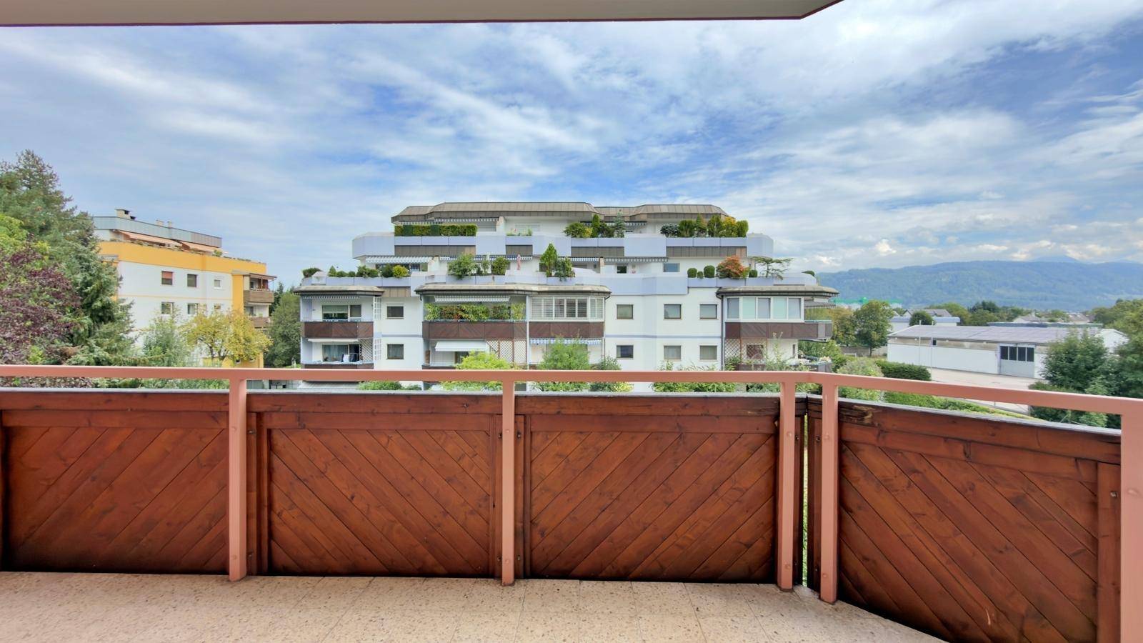 Balkon mit Holzbalkonbrüstung und Ausblick auf die umliegenden Gebäude und die Berglandschaft.
