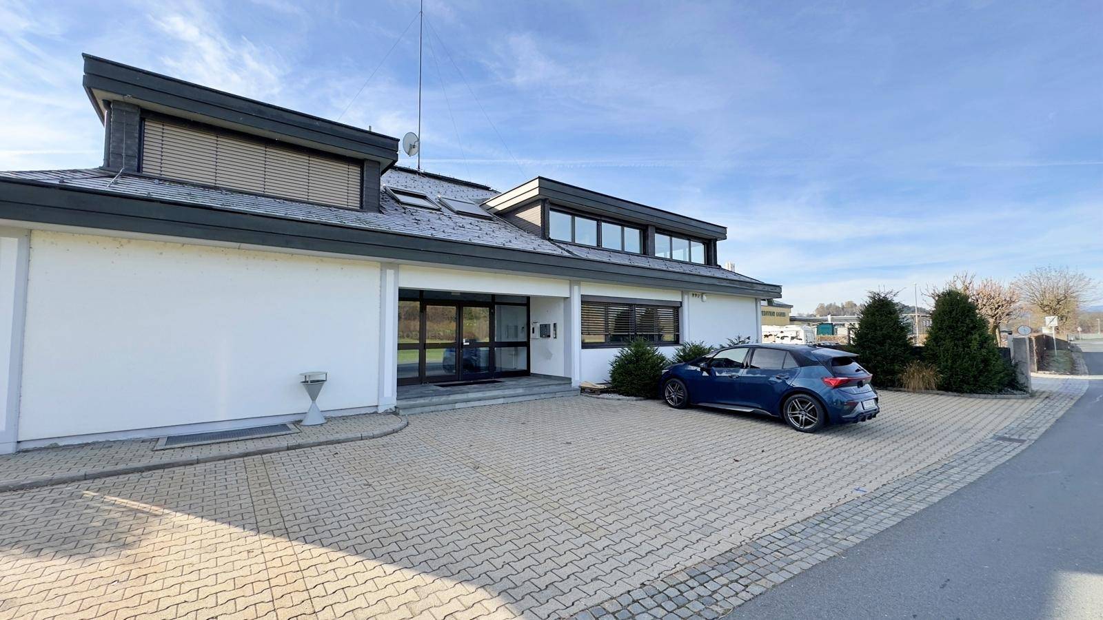 Außenansicht des modernen Bürogebäudes mit gepflastertem Parkplatz und einem geparkten blauen Auto.