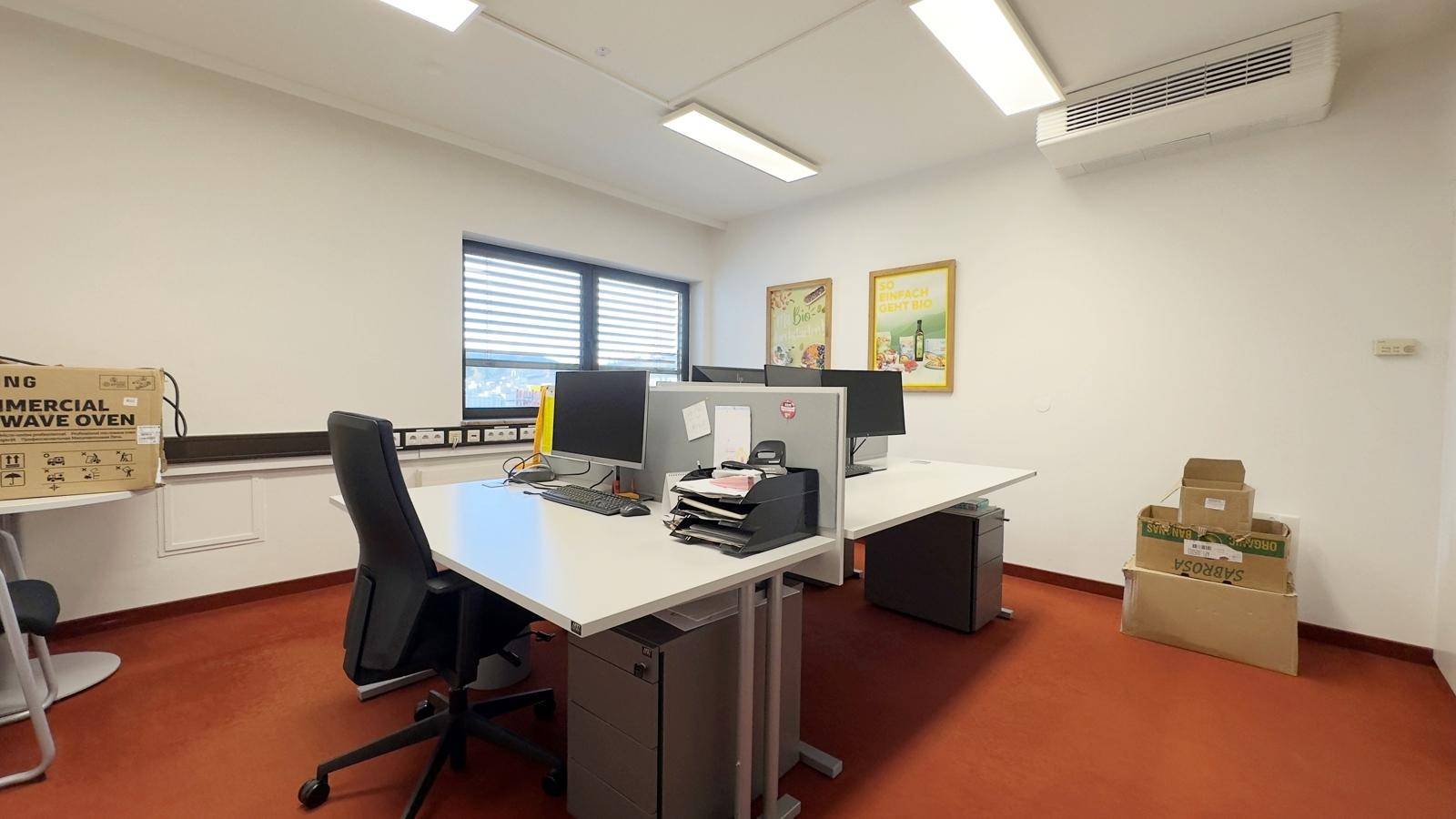 Büroarbeitsplatz mit Computern, Schreibtischen, Bürostühlen und einem orangefarbenen Teppichboden.