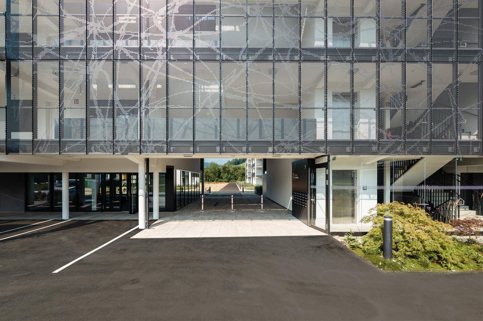 Moderne Gebäudefassade mit perforierter Metallverkleidung und Zufahrt zum Parkplatz.