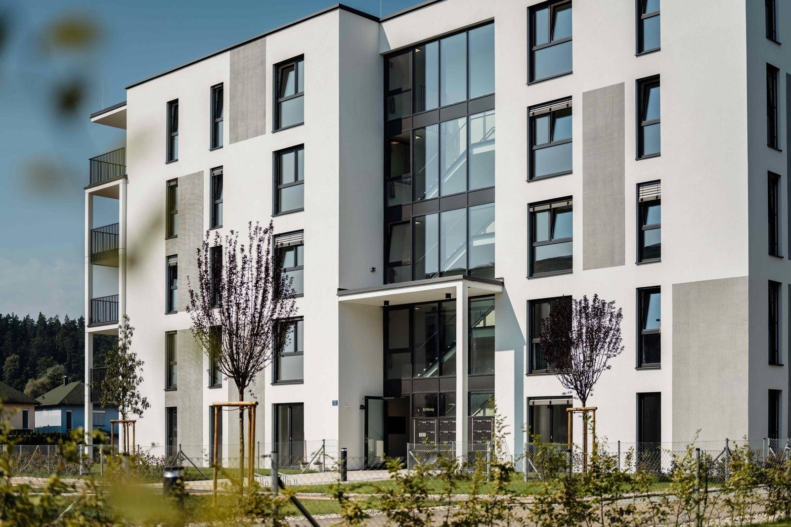Nahaufnahme eines modernen Wohngebäudes mit großen Glasflächen im Eingangsbereich und schlichten Fassadenelementen.