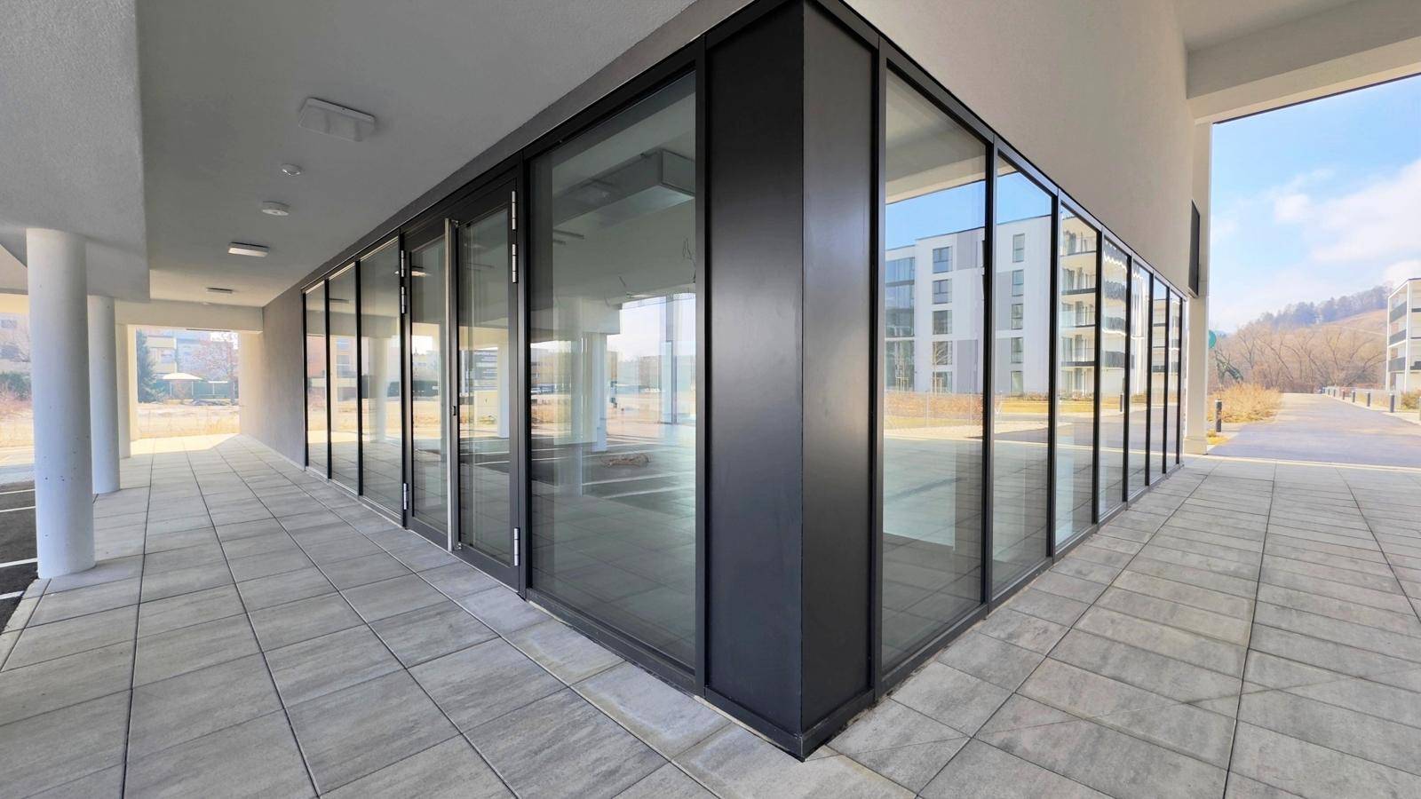 Außenansicht eines modernen Geschäftsgebäudes mit großen Fensterfronten und grauem Gehweg.