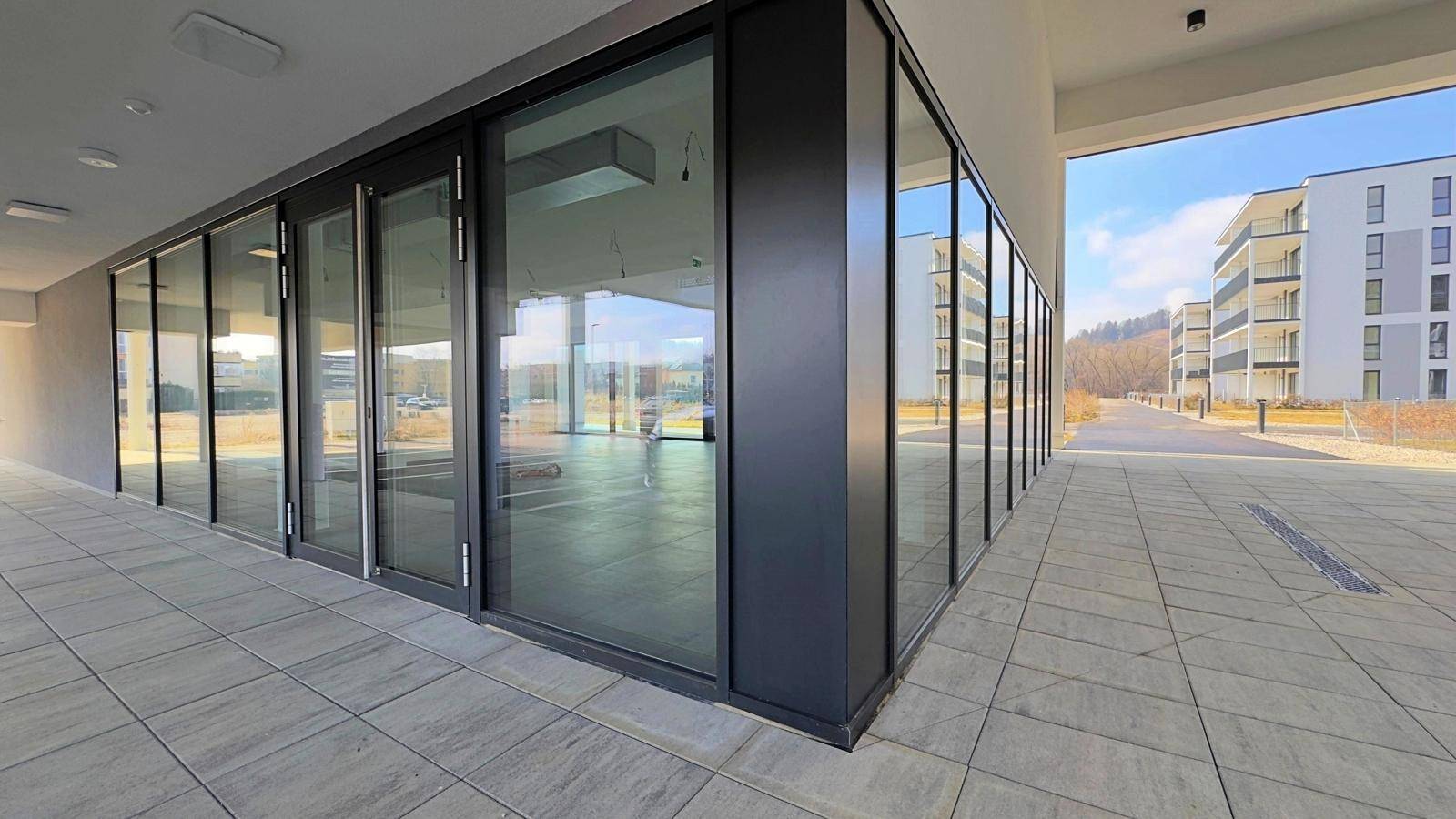 Moderne Geschäftsfläche im Erdgeschoss mit durchgehender Glasfront und heller Außenbeleuchtung.