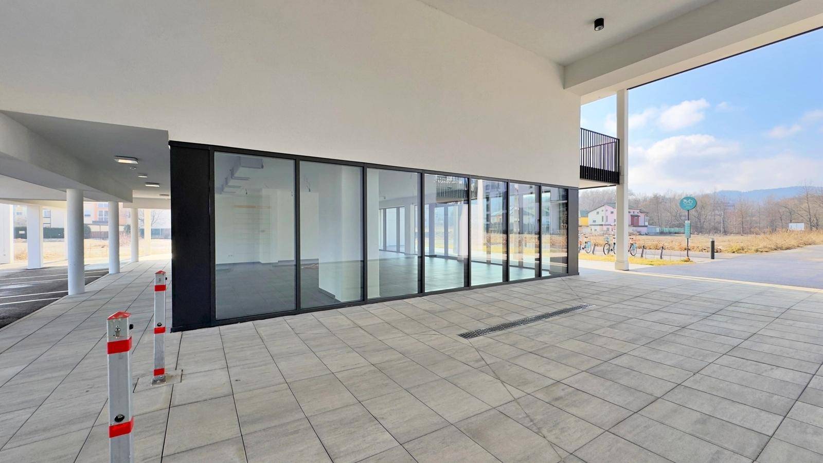 Weitläufige Außenansicht einer modernen Gewerbefläche mit großen Schaufenstern und gepflastertem Vorplatz.