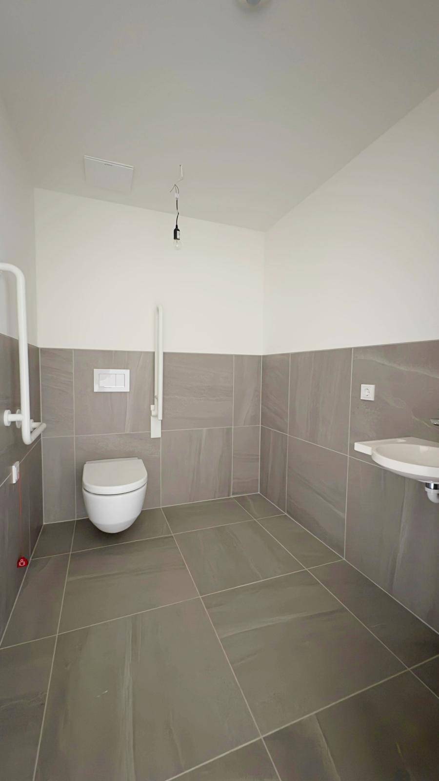 Barrierefreies Badezimmer mit Haltegriffen, wandhängender Toilette und Waschbecken.