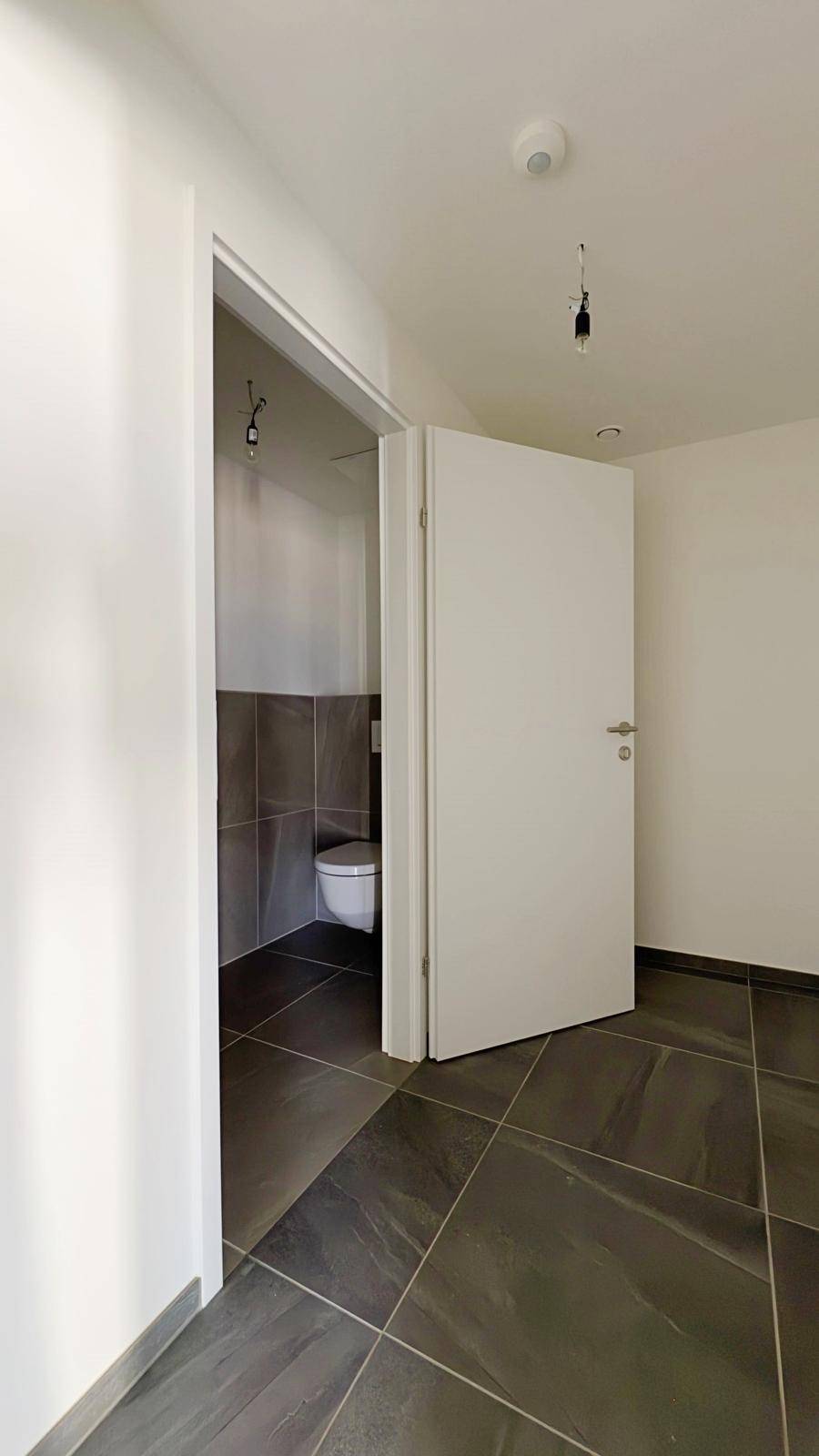 Badezimmer mit wandhängender Toilette und grauen Fliesen, bereit für die Endmontage.