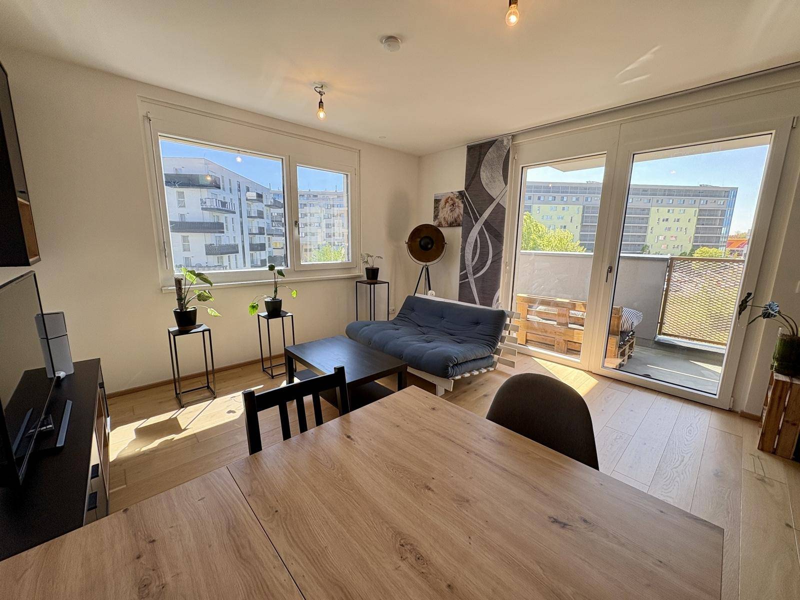 Lichtdurchfluteter Wohn- und Essbereich mit Holzboden und direktem Zugang zum Balkon.