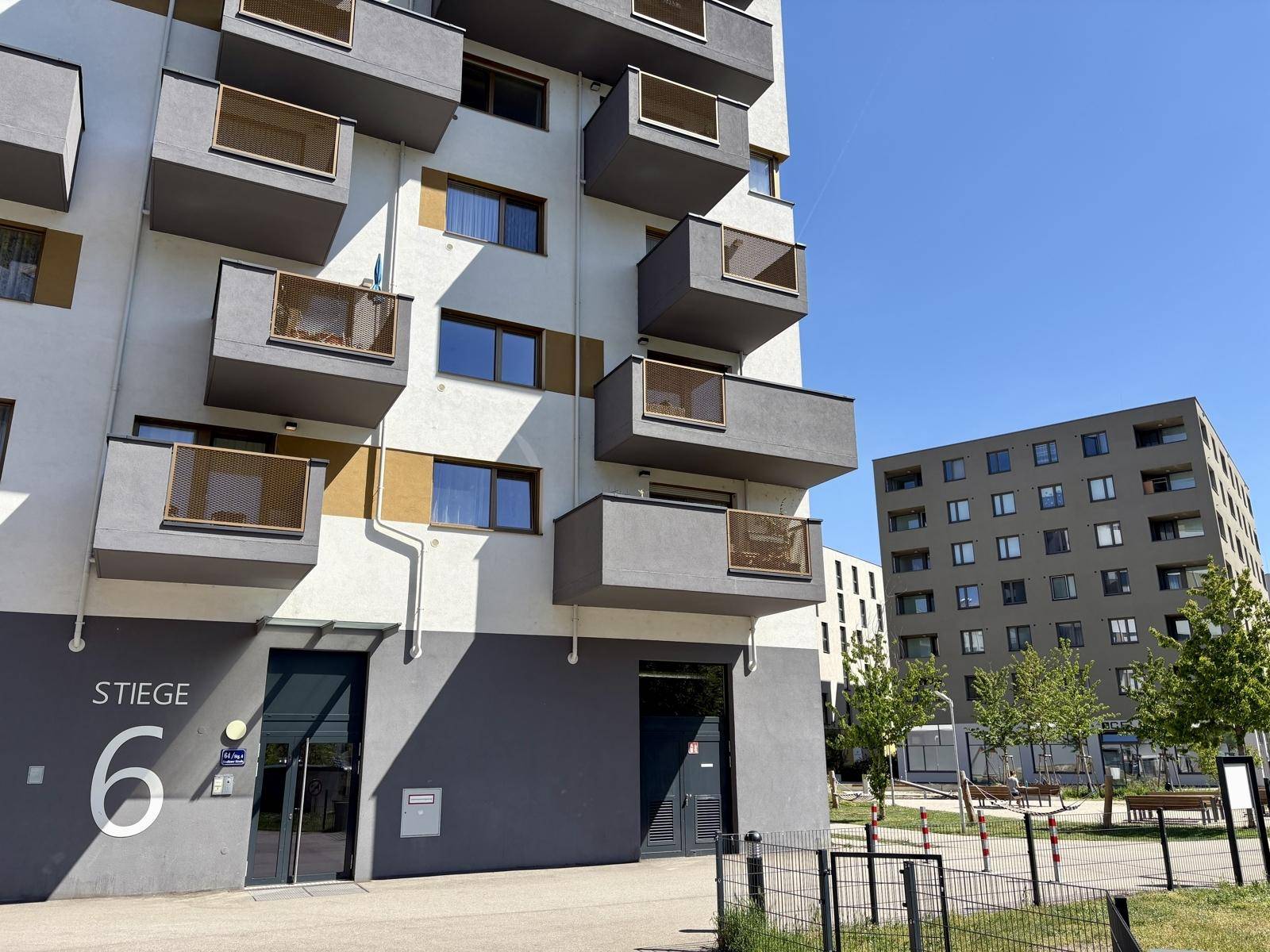 Eingangsbereich eines modernen Mehrfamilienhauses mit Balkonen und der Aufschrift "Stiege 6".