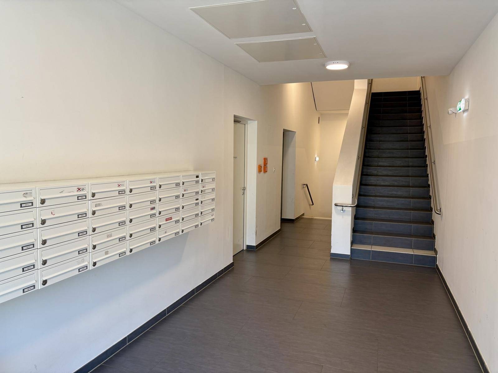 Heller Eingangsbereich eines Mehrfamilienhauses mit Briefkästen und Treppenaufgang.
