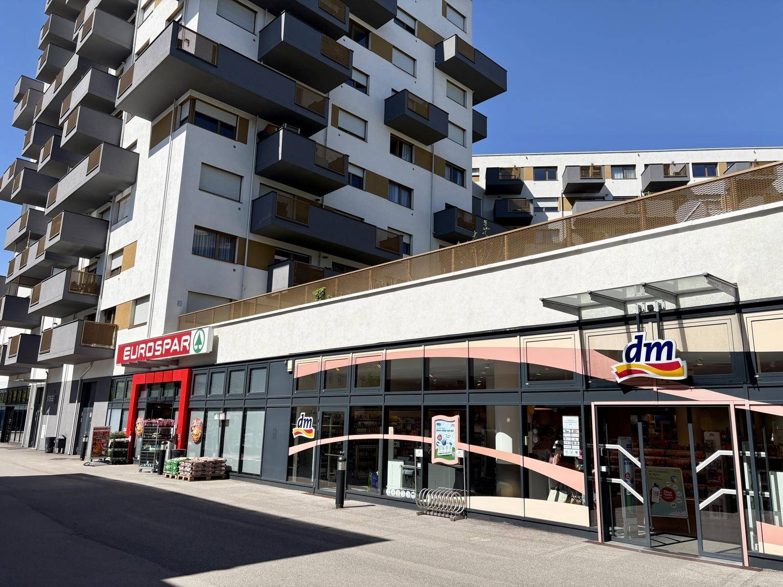 Moderne Geschäftsfassade mit Supermarkt und Drogerie im Erdgeschoss eines Wohngebäudes.