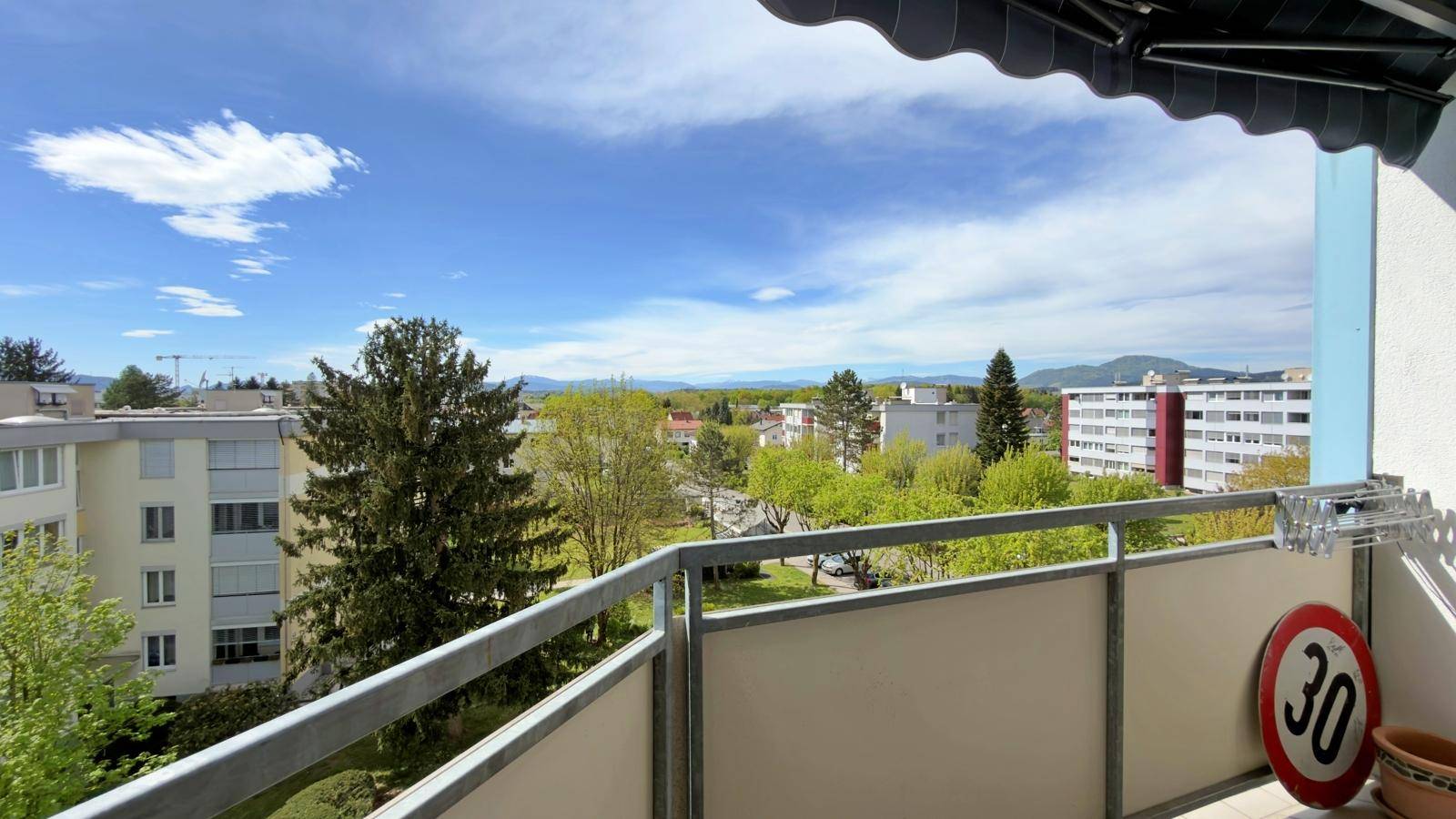Balkon mit Metallgeländer und Markise, bietet eine weite Aussicht auf die Stadt und die Berge.