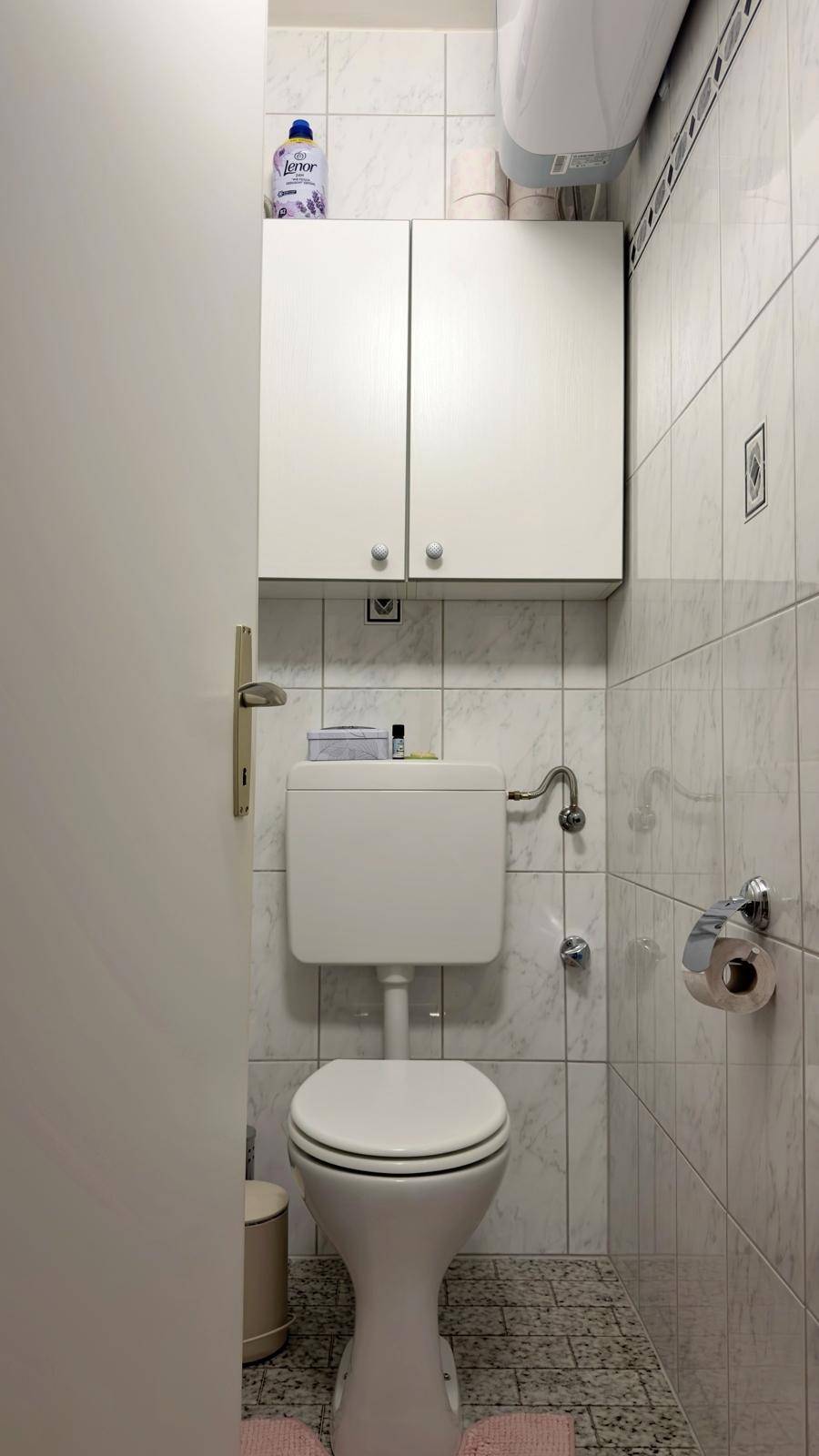 Separates WC mit Toilette, Wandfliesen und kleinem Hängeschrank.
