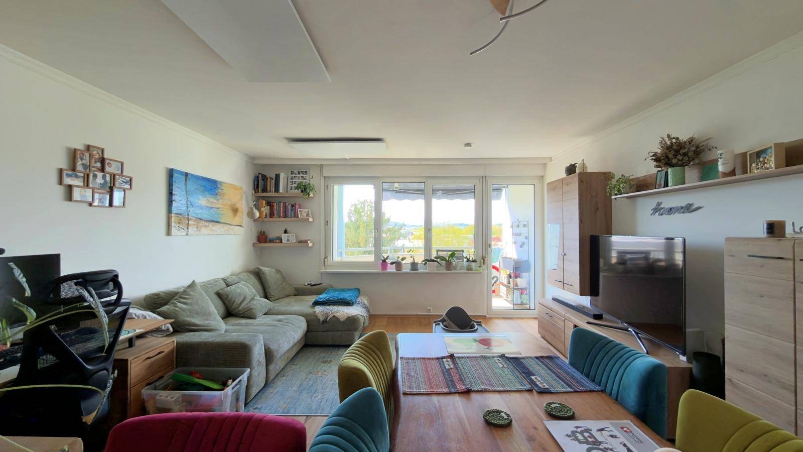 Geräumiger Wohn-Essbereich mit bequemer Couch, Esstisch und Blick ins Grüne durch große Fenster.