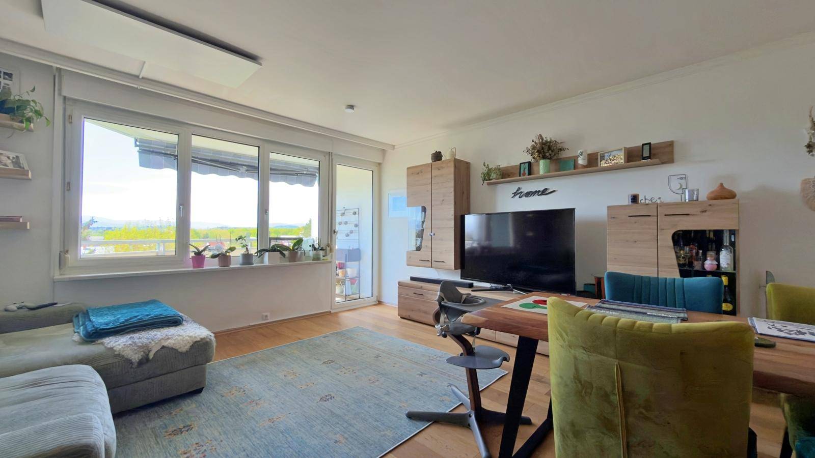 Wohnbereich mit Sofa, TV-Möbeln und großen Fenstern, die viel Tageslicht hereinlassen.
