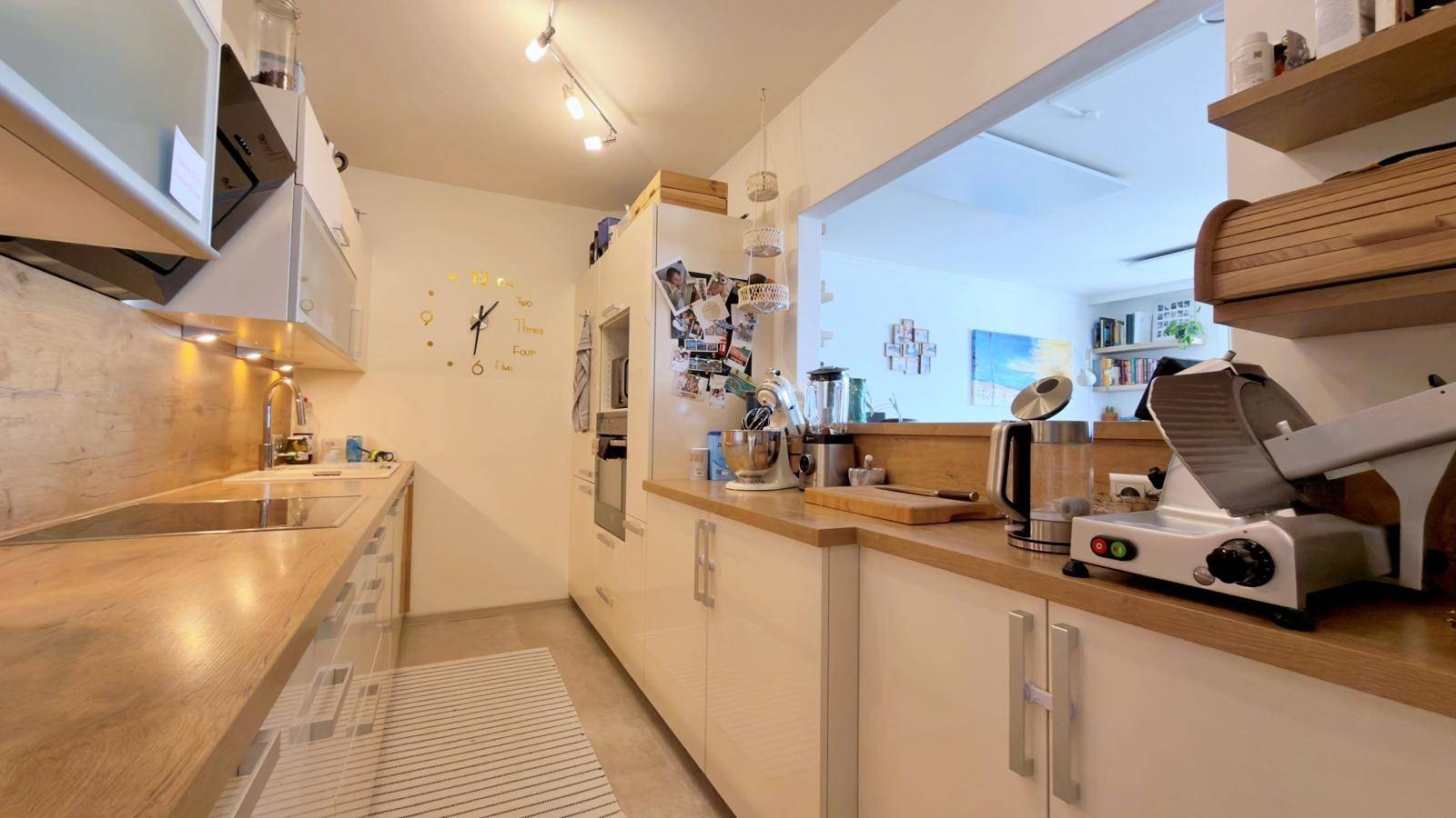 Moderne Küche mit hellen Schränken, Holz-Arbeitsplatten und praktischer Durchreiche zum Wohnbereich.