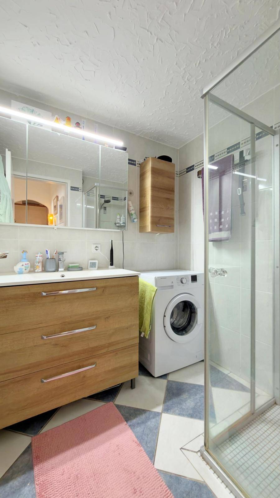 Badezimmer mit Duschkabine, Einzelwaschbecken und integrierter Waschmaschine.
