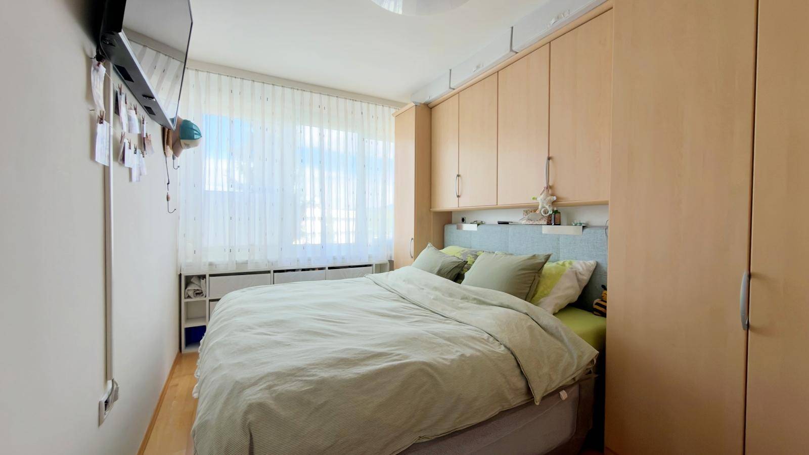 Schlafzimmer mit Doppelbett, integrierten Holzschränken und hellem Fenster mit Vorhängen.